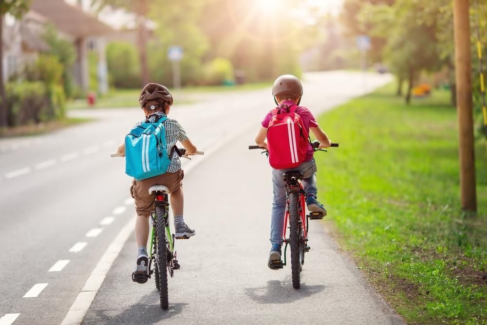Two school boys wearing backpacks riding bicycles to school on the road