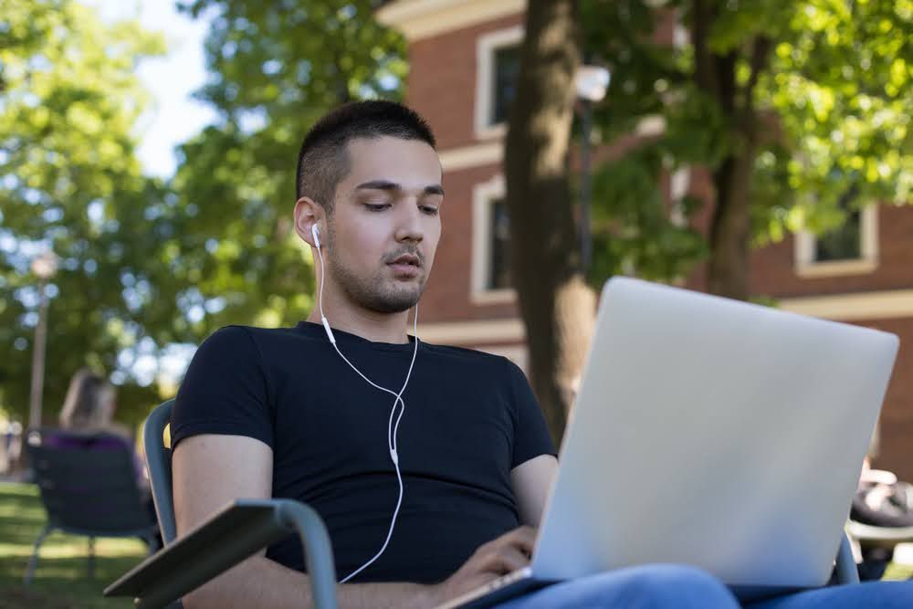 Young man outdoors sitting in a chair with laptop applying for California e-bike rebate