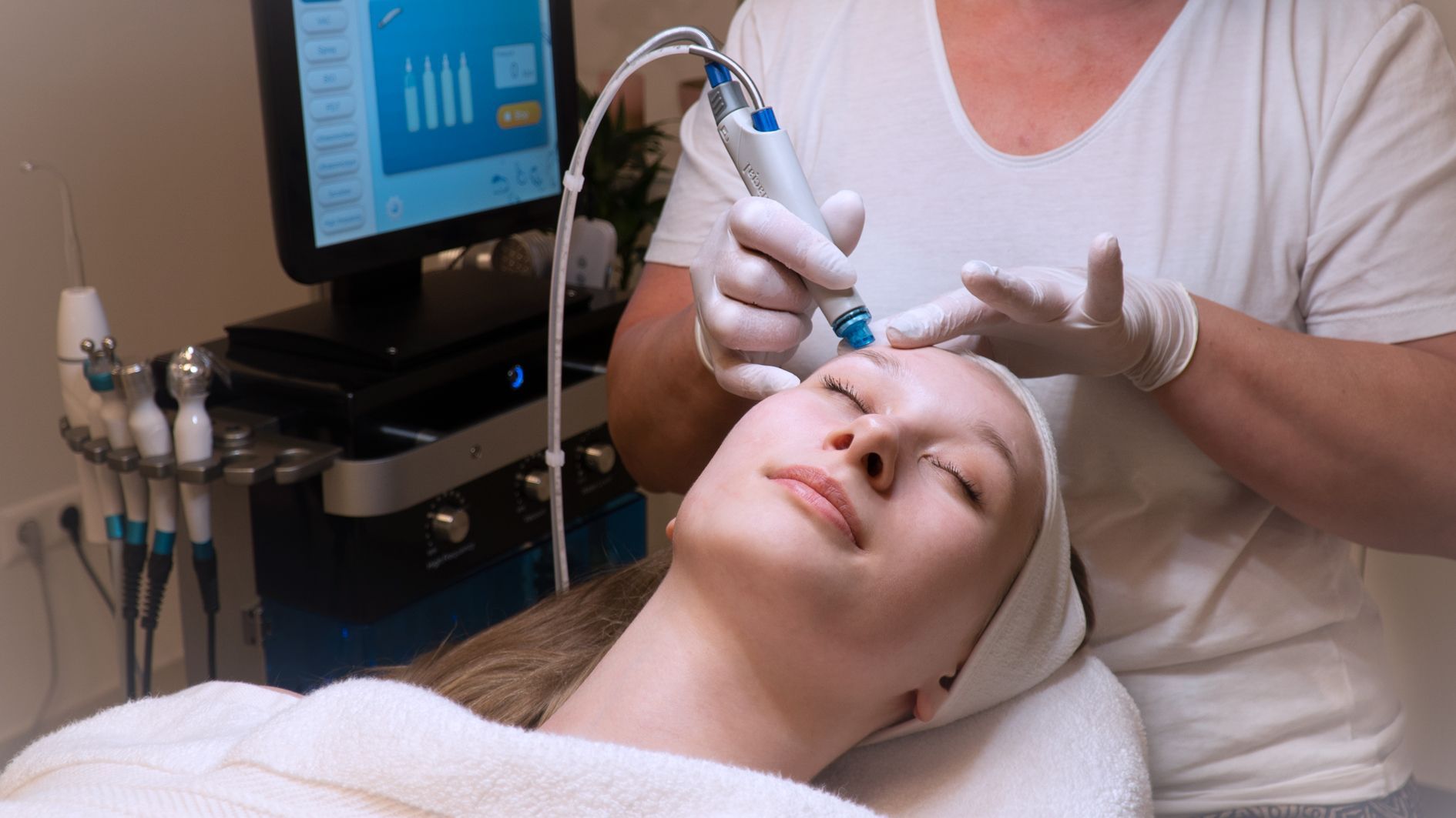 Frau erhält eine Gesichtsbehandlung; ein Techniker verwendet ein Gerät an ihrer Stirn; Spa-Umgebung.