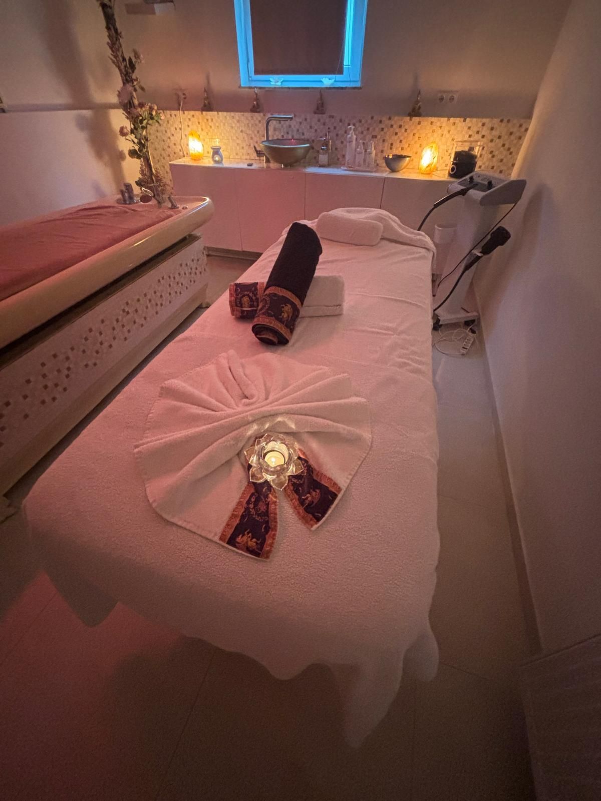 Massageraum mit vorbereiteter Liege, Handtüchern und stimmungsvoller Beleuchtung.