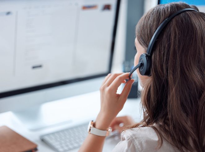 A woman wearing a headset is sitting in front of a computer.