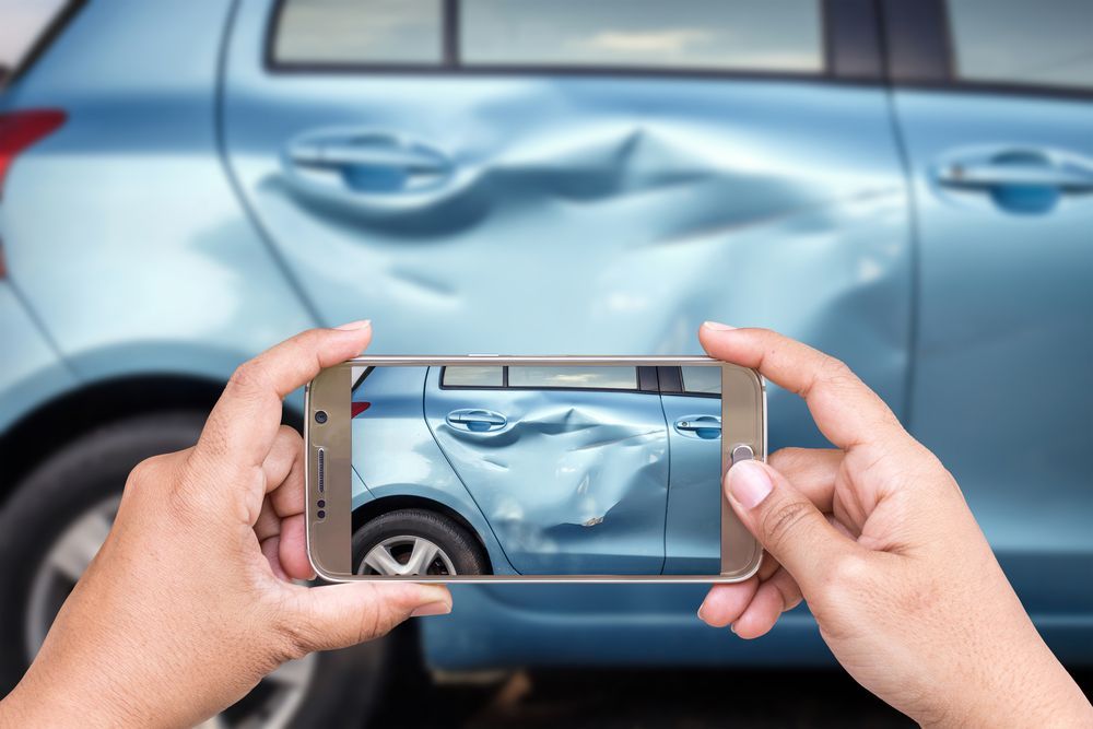 A person is taking a picture of a damaged car with a cell phone.