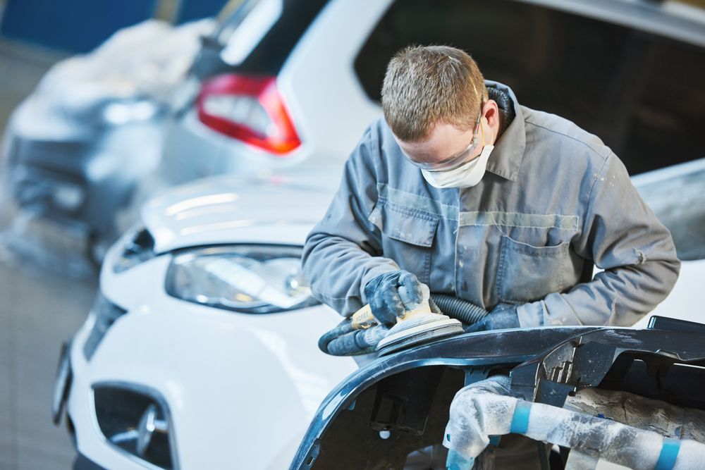 A man wearing a mask is sanding a car fender in a garage.