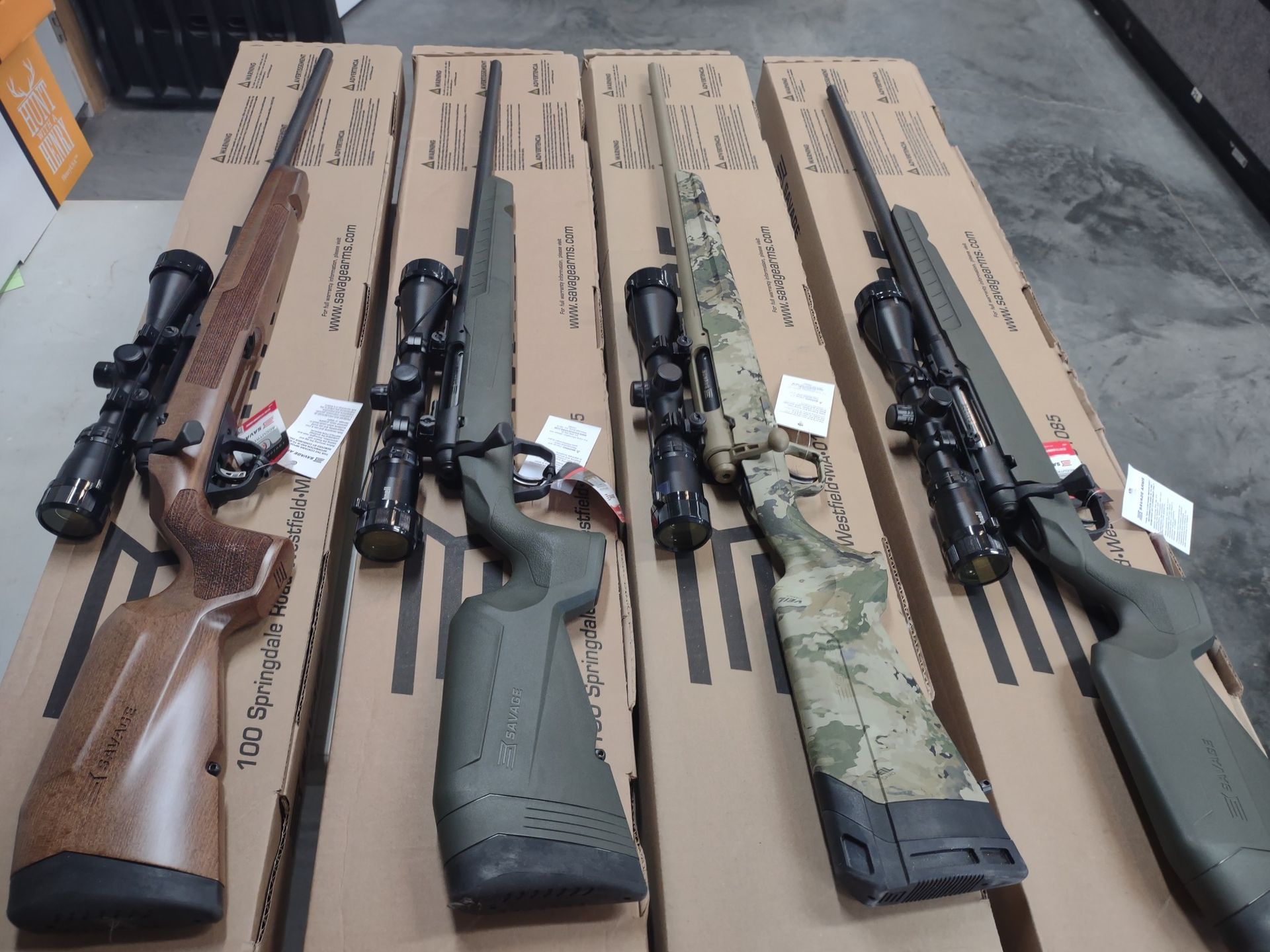 Four rifles with scopes, in cases, various finishes, likely for sale.