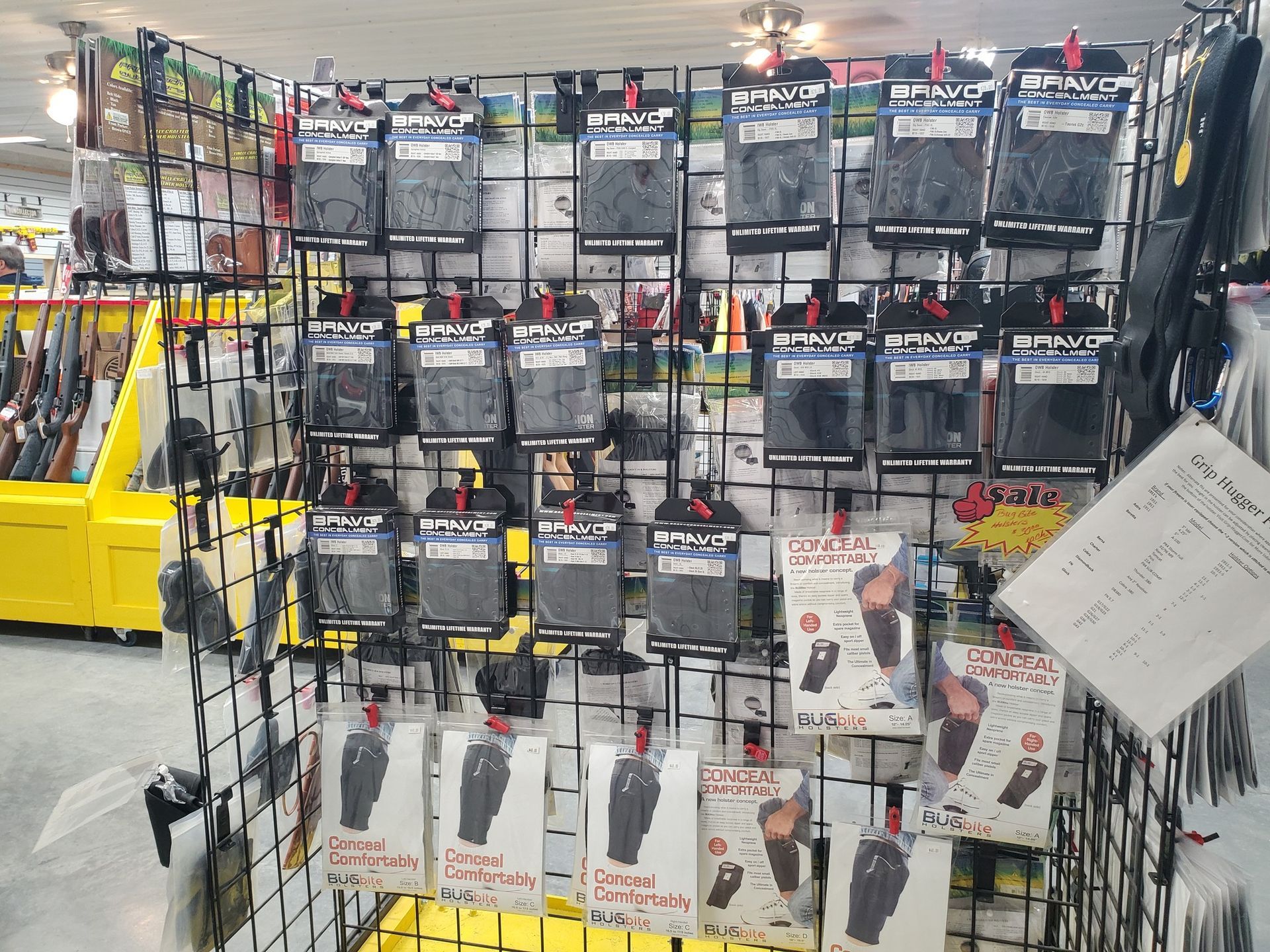 Display of packaged holsters for sale in a store, hanging on a black wire grid.