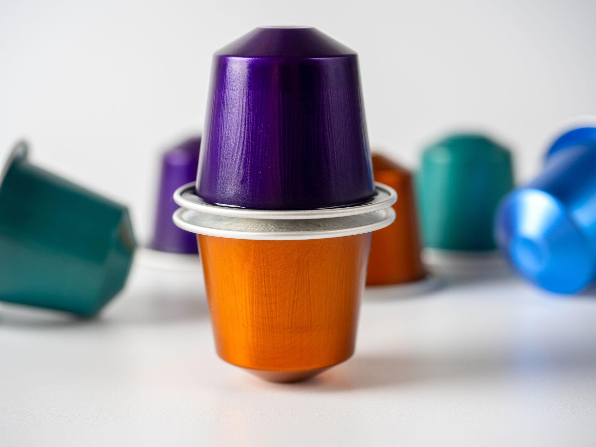Capsule di caffè Nespresso colorate impilate su una superficie bianca; in primo piano le cialde arancioni e viola.