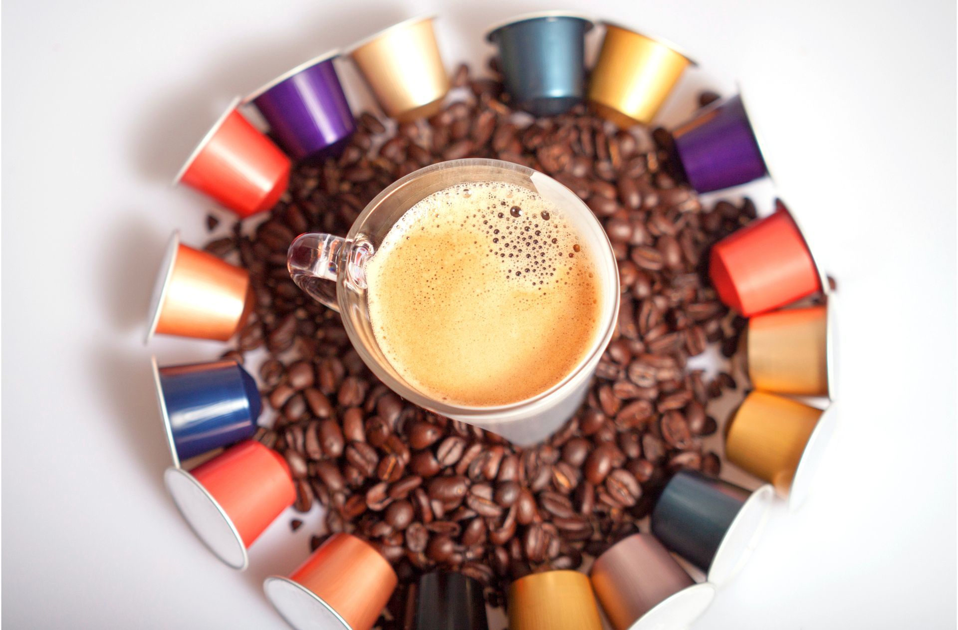 Caffè in una tazza di vetro circondata da chicchi tostati e cialde di caffè colorate.