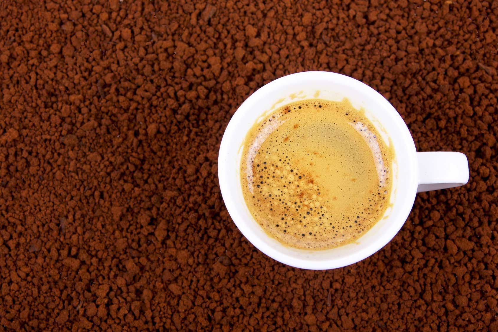 Caffè in una tazza bianca su un letto di granuli di caffè istantaneo, ripresa dall'alto.