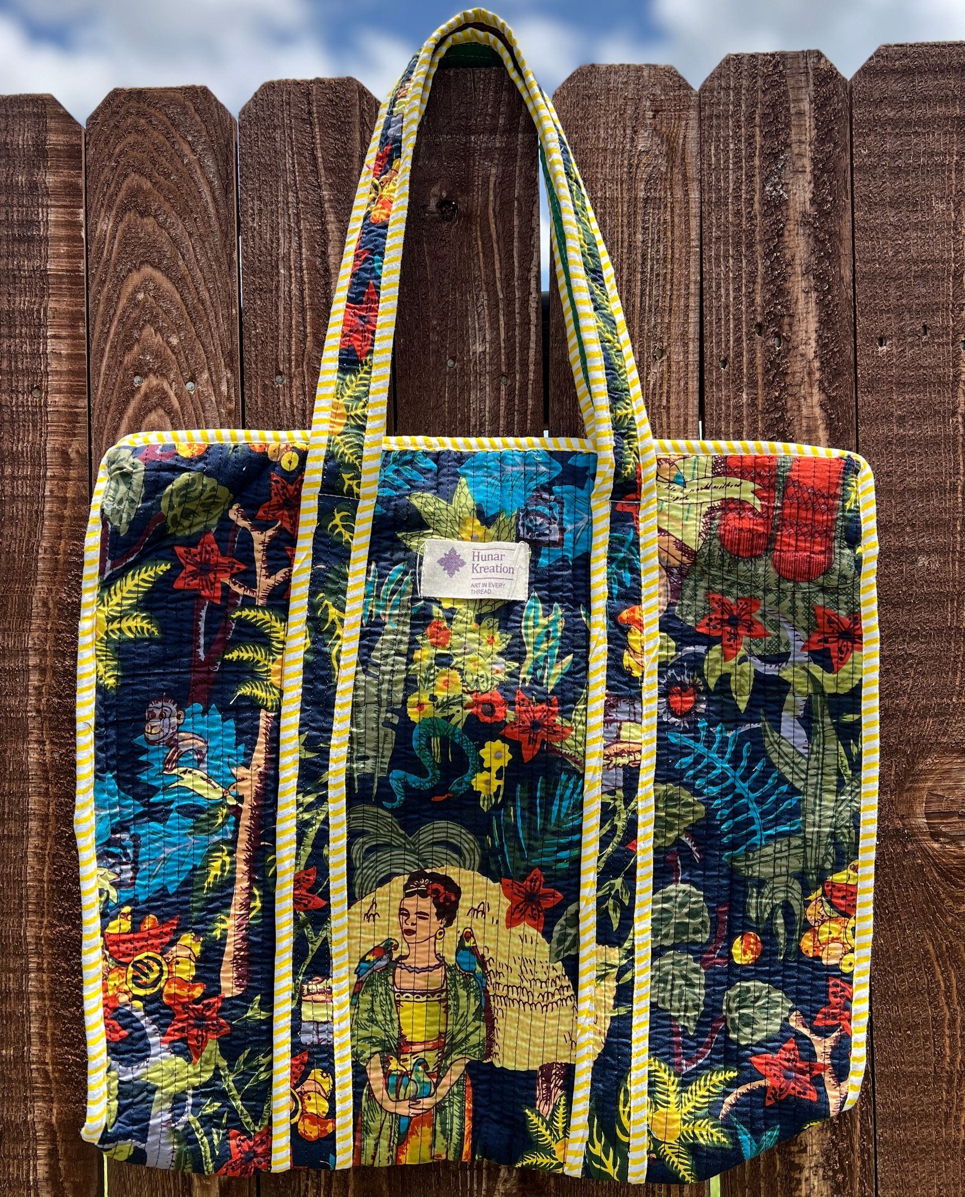 A colorful tote bag is hanging on a wooden fence.