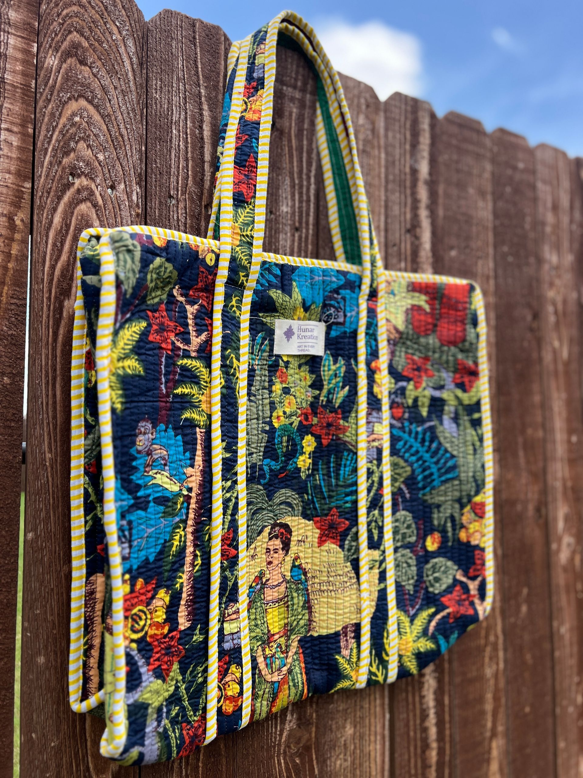A colorful tote bag is hanging on a wooden fence.
