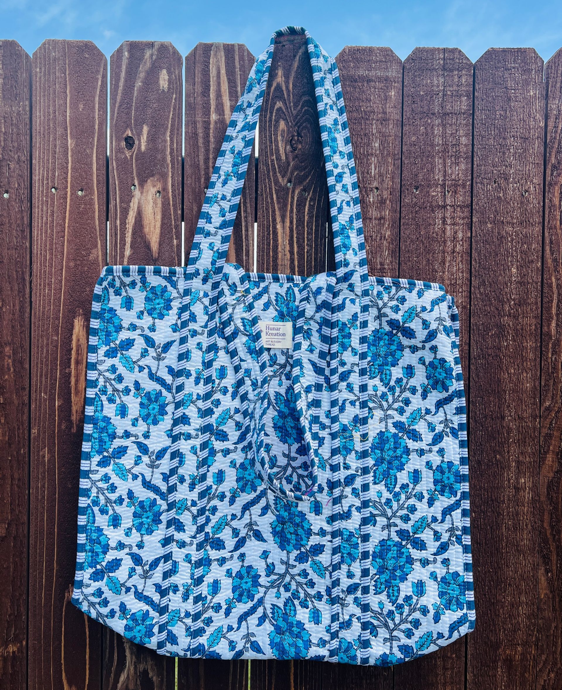 A blue and white tote bag is hanging on a wooden fence.