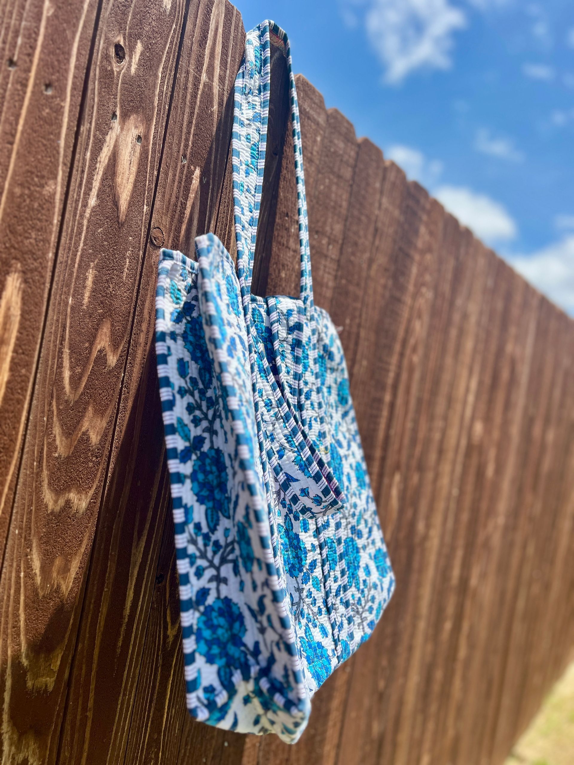 A blue and white tote bag is hanging on a wooden fence.