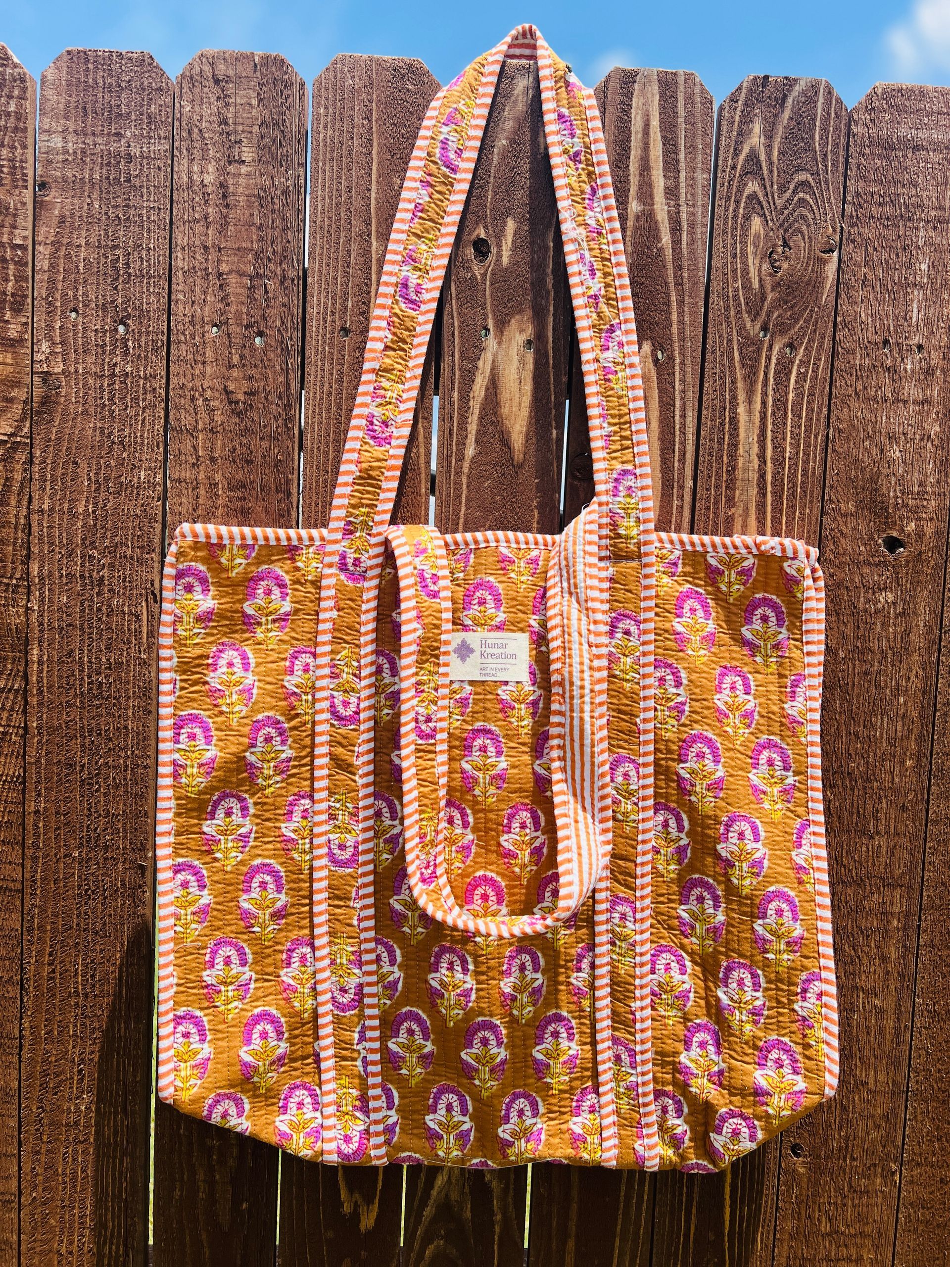 A colorful tote bag is hanging on a wooden fence.