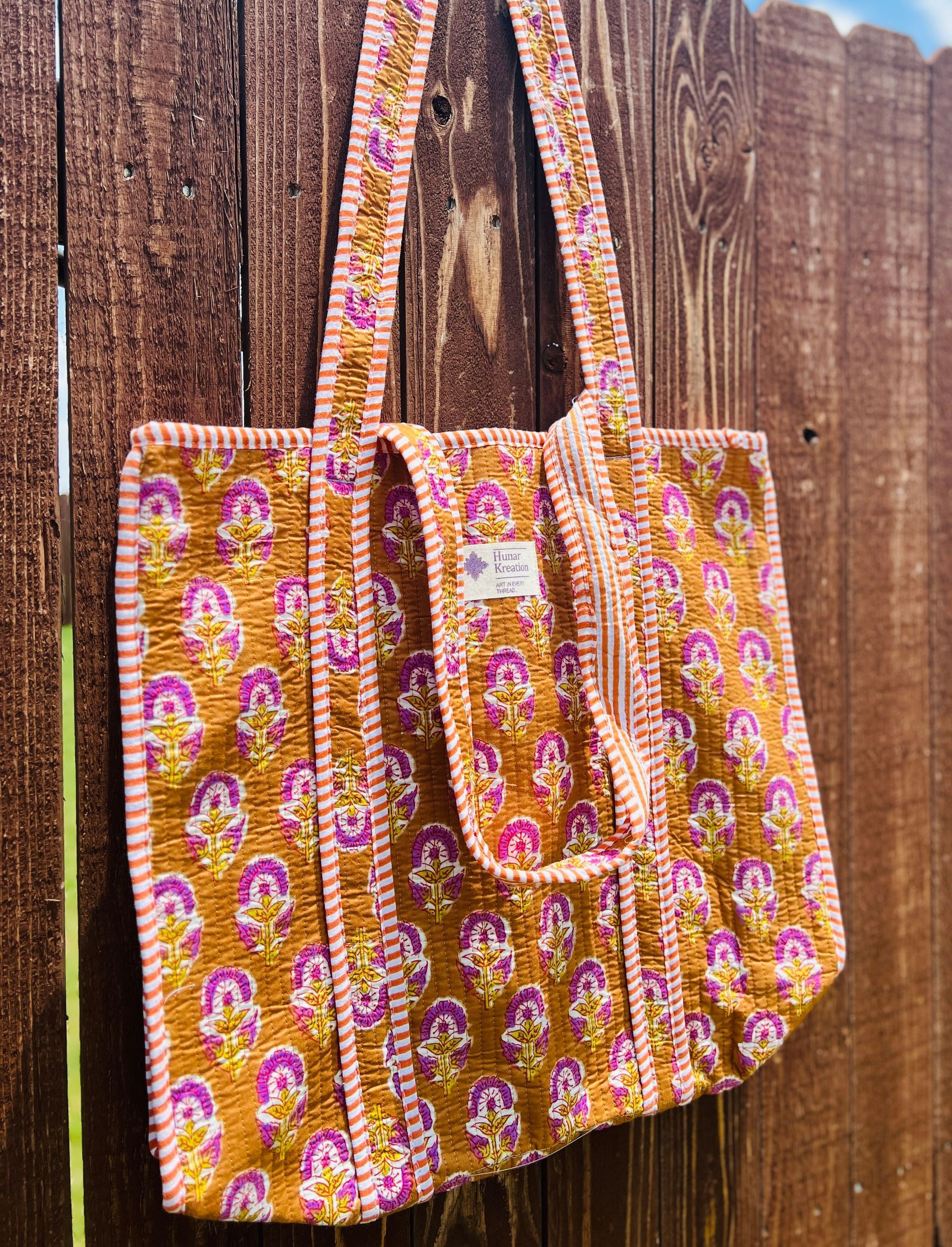 A colorful tote bag is hanging on a wooden fence.