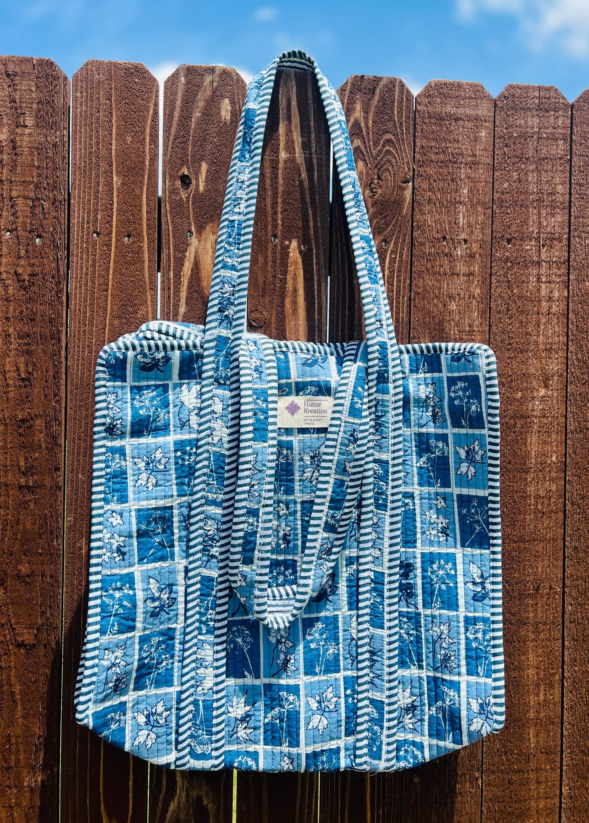 A blue and white tote bag is hanging on a wooden fence.