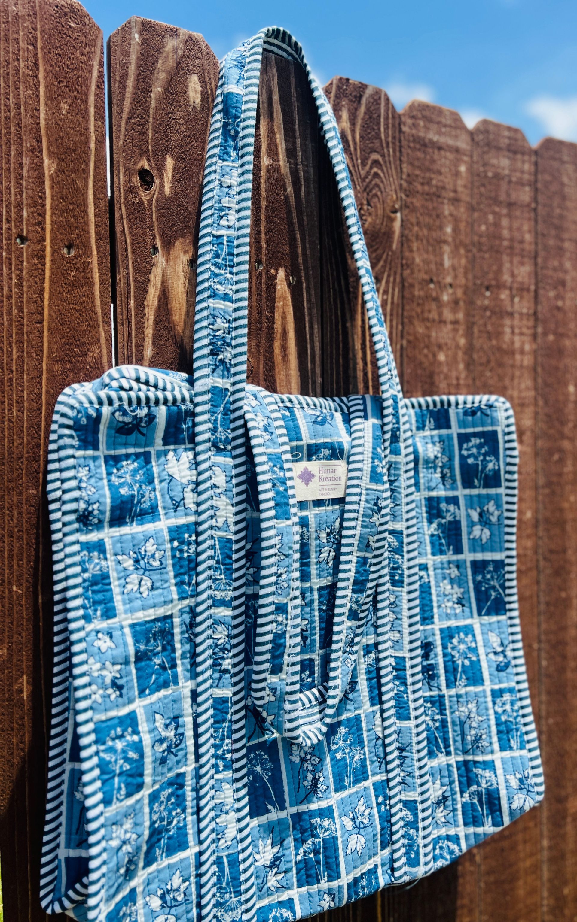 A blue and white tote bag is hanging on a wooden fence.