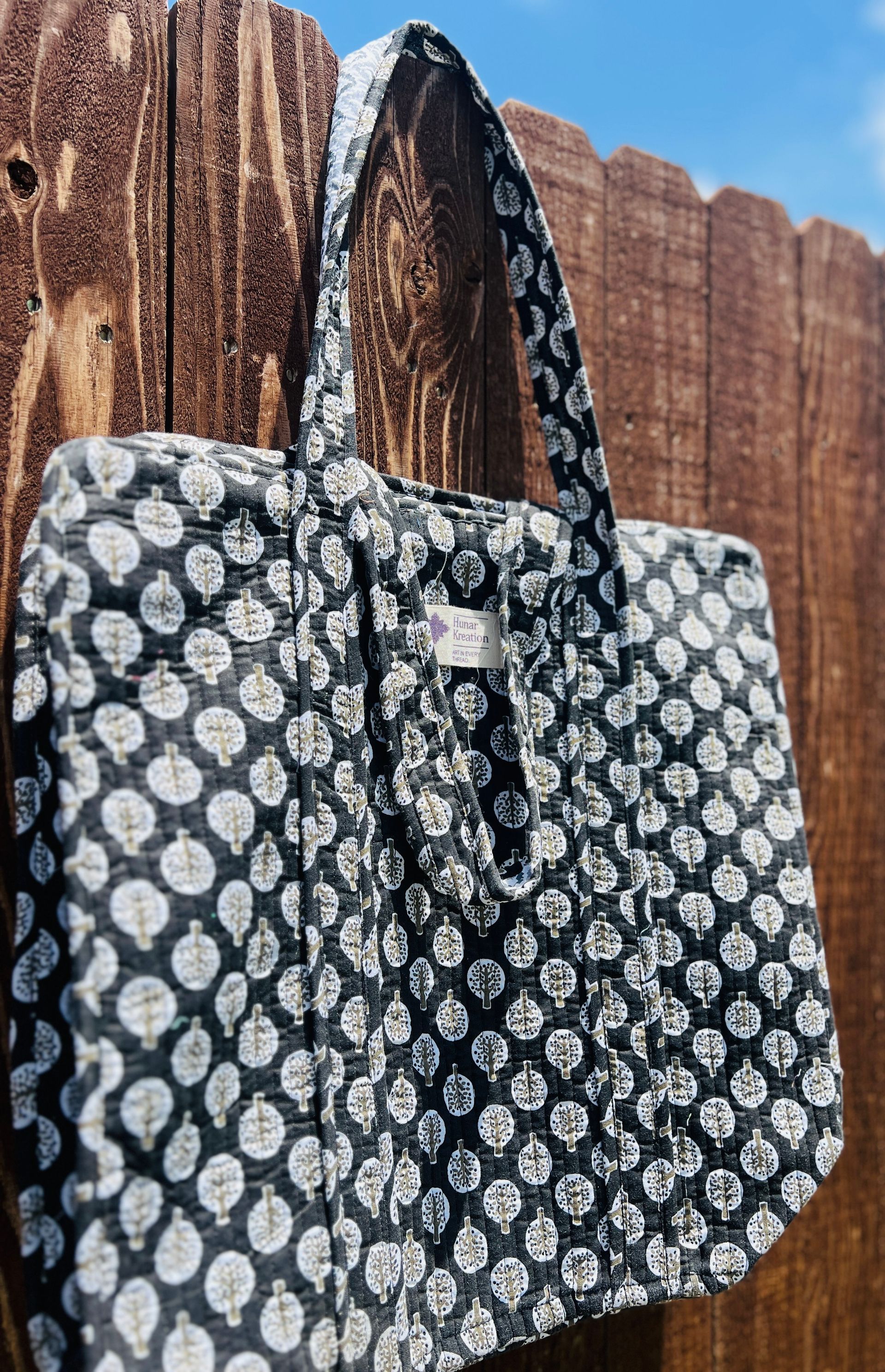 A black and white polka dot tote bag is hanging on a wooden fence.