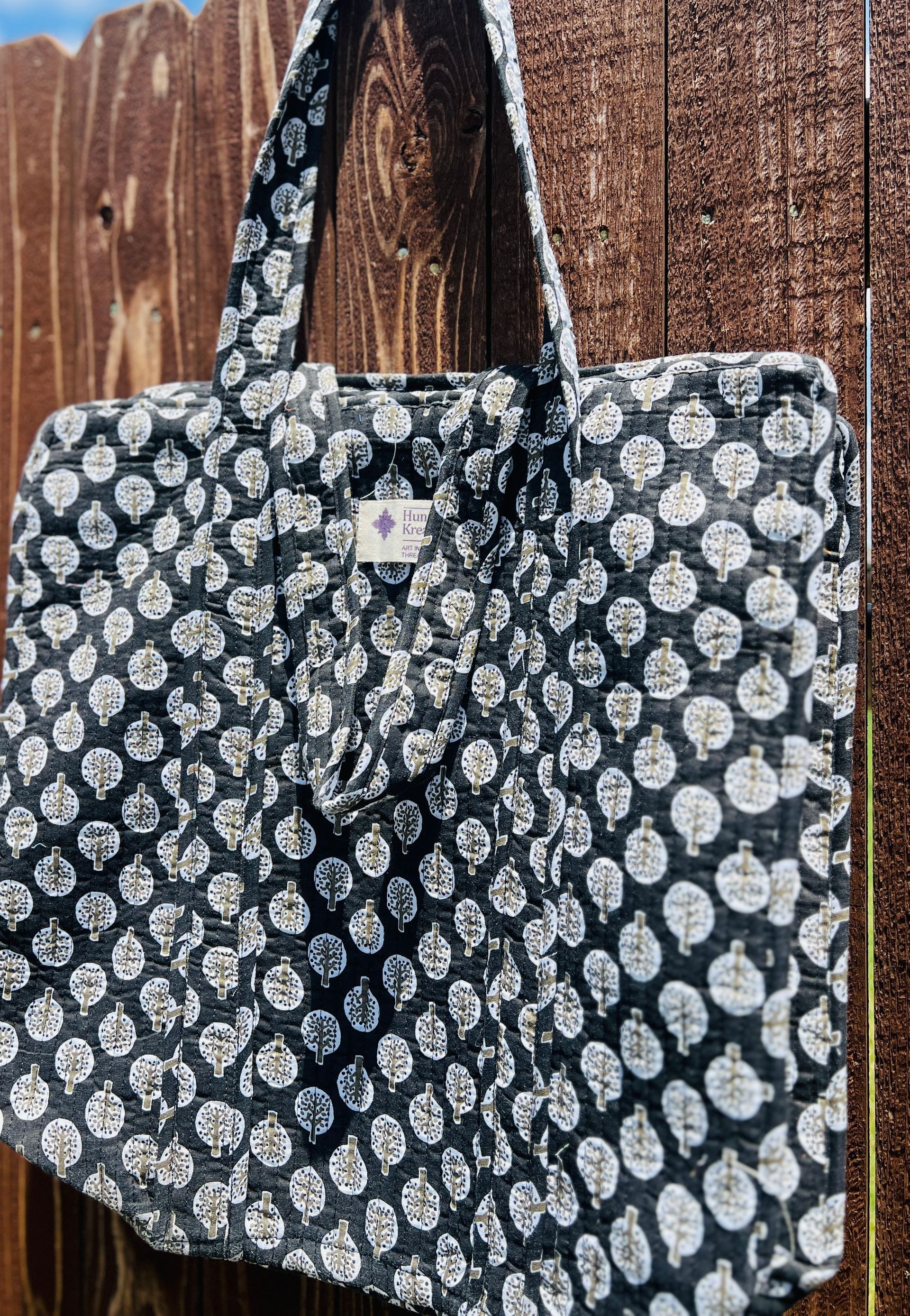 A black and white polka dot tote bag is hanging on a wooden fence.