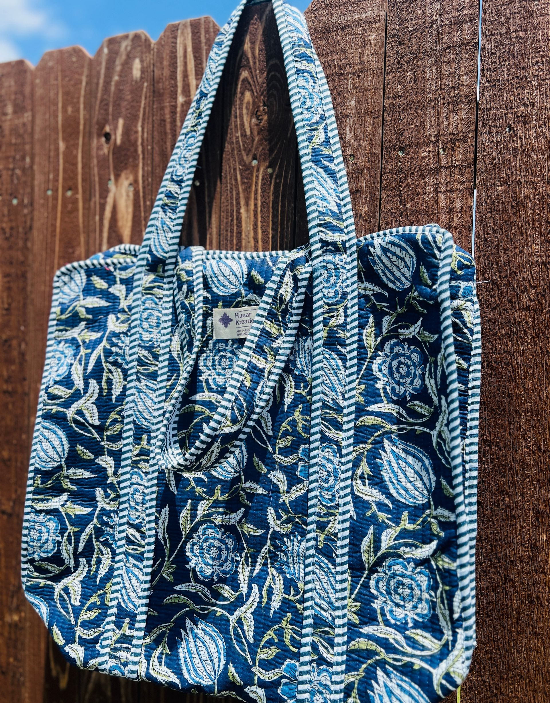 A blue and white tote bag is hanging on a wooden fence