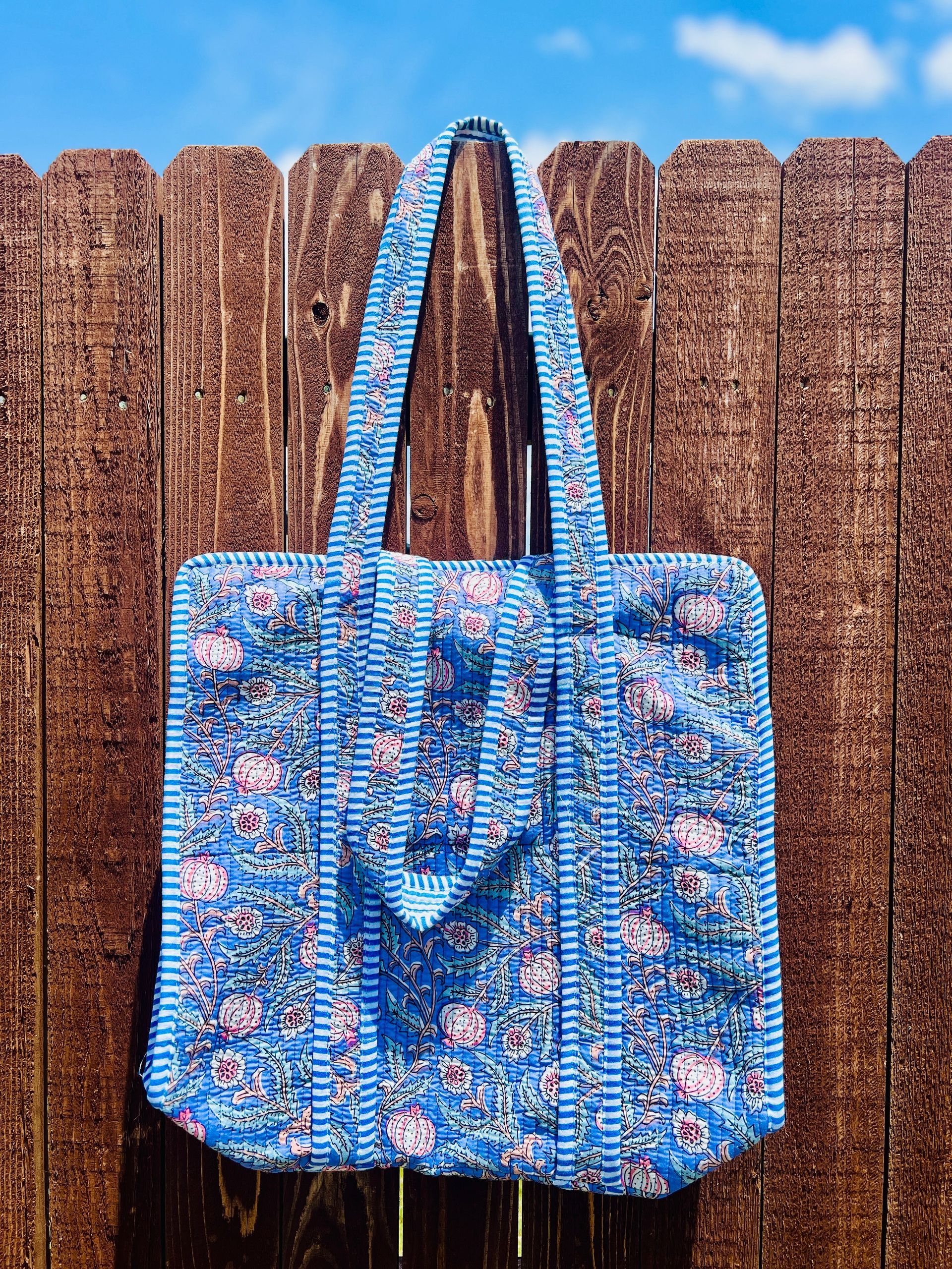 A blue floral tote bag is hanging on a wooden fence