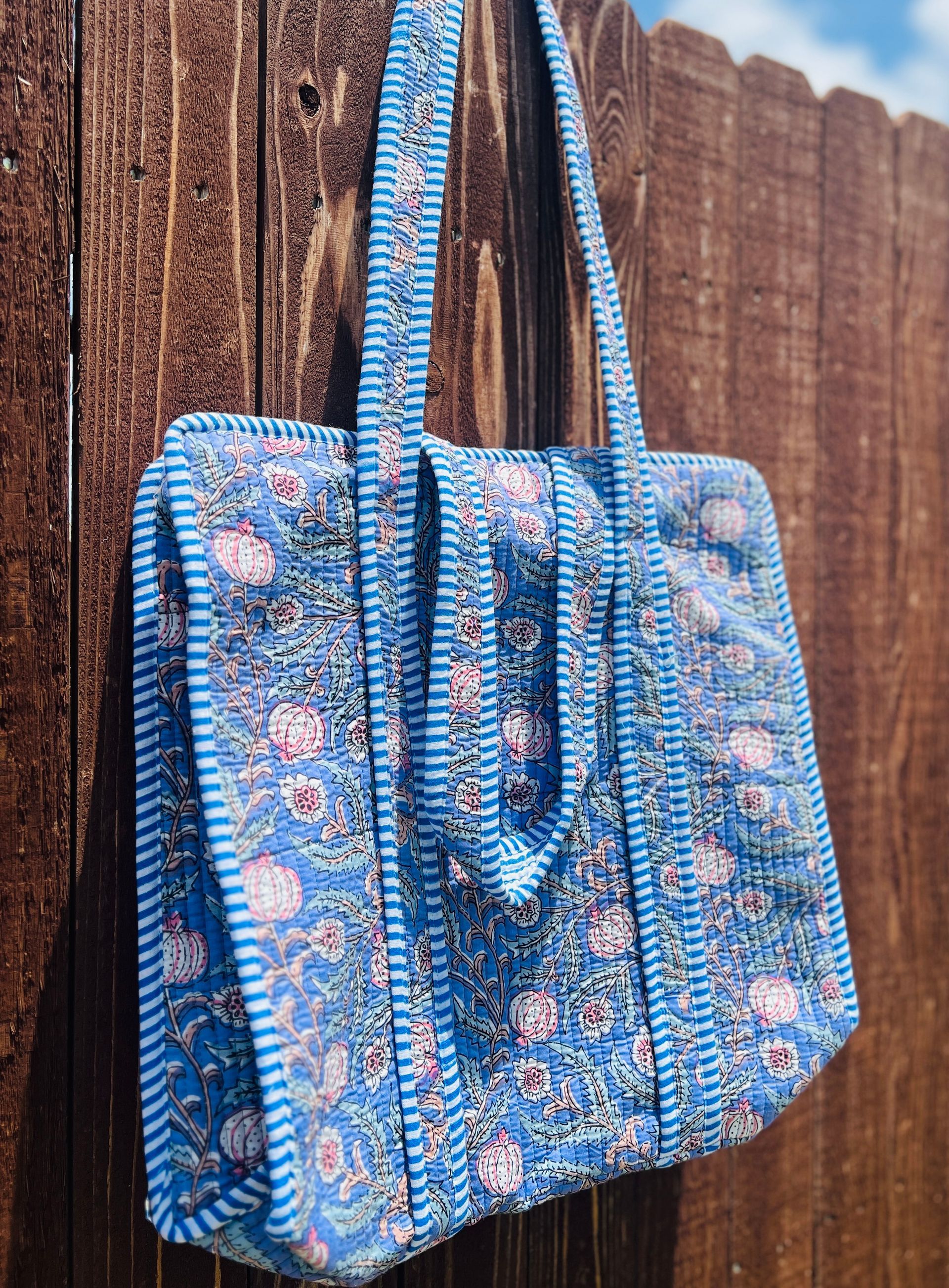 A blue floral tote bag is hanging on a wooden fence