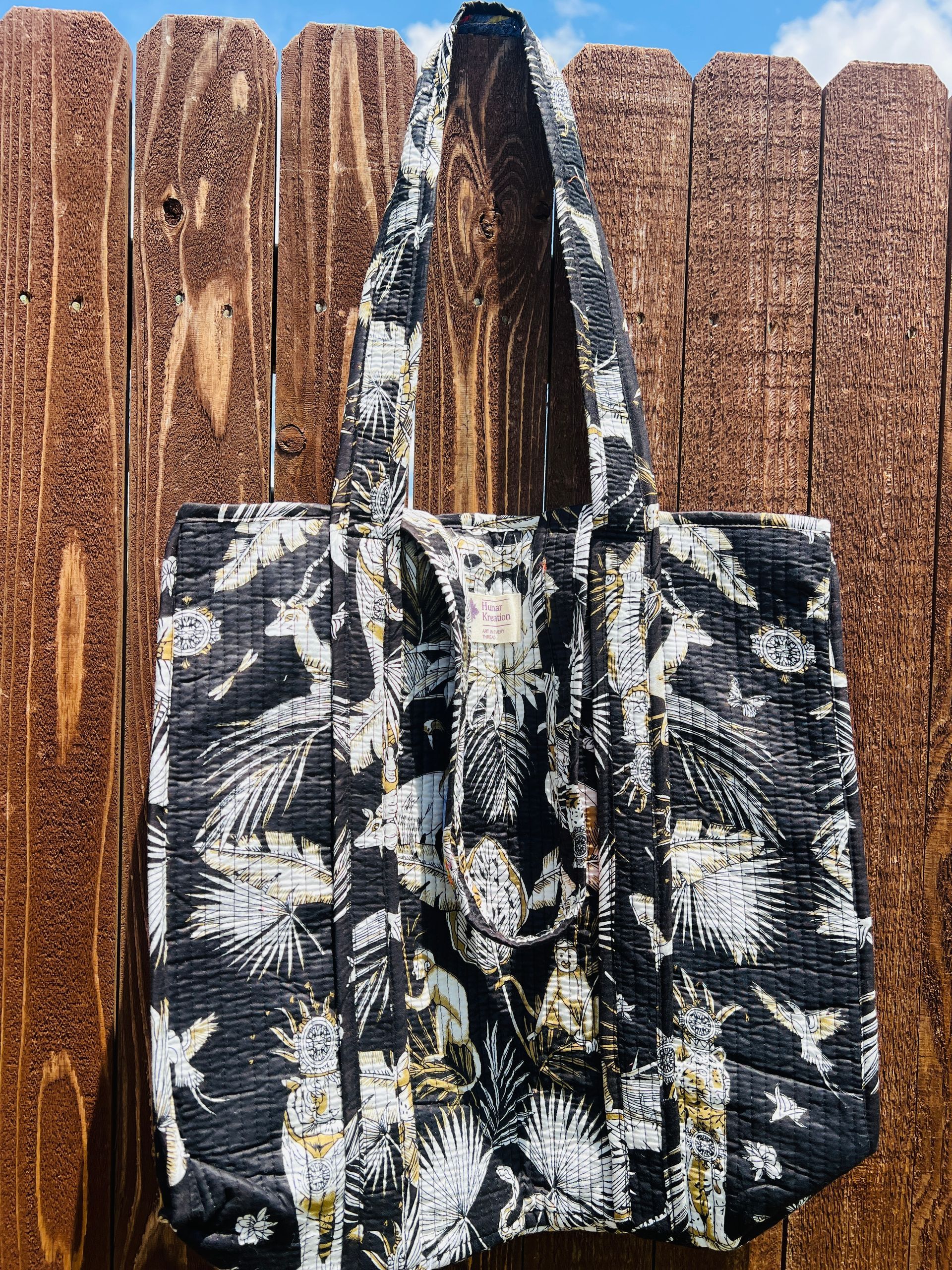 A black and white tote bag is hanging on a wooden fence.