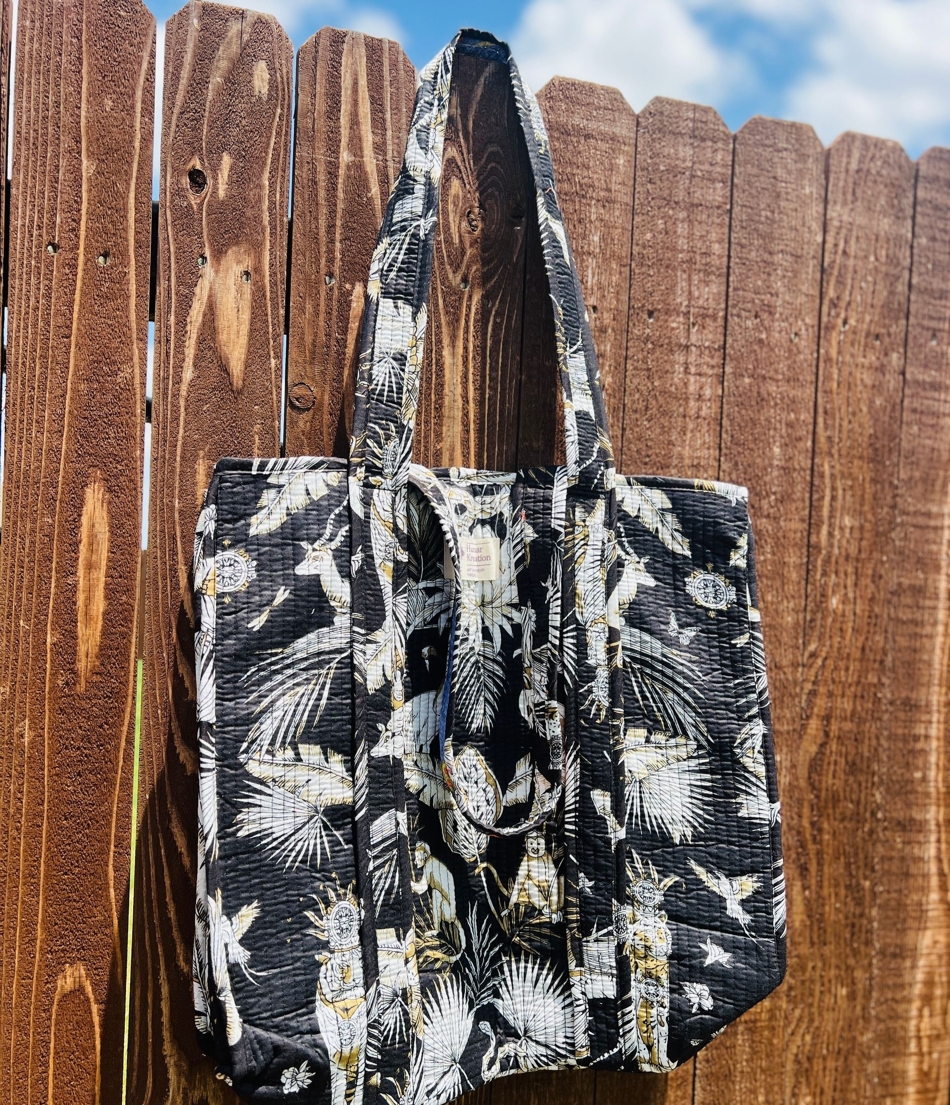 A black and white tote bag is hanging on a wooden fence.