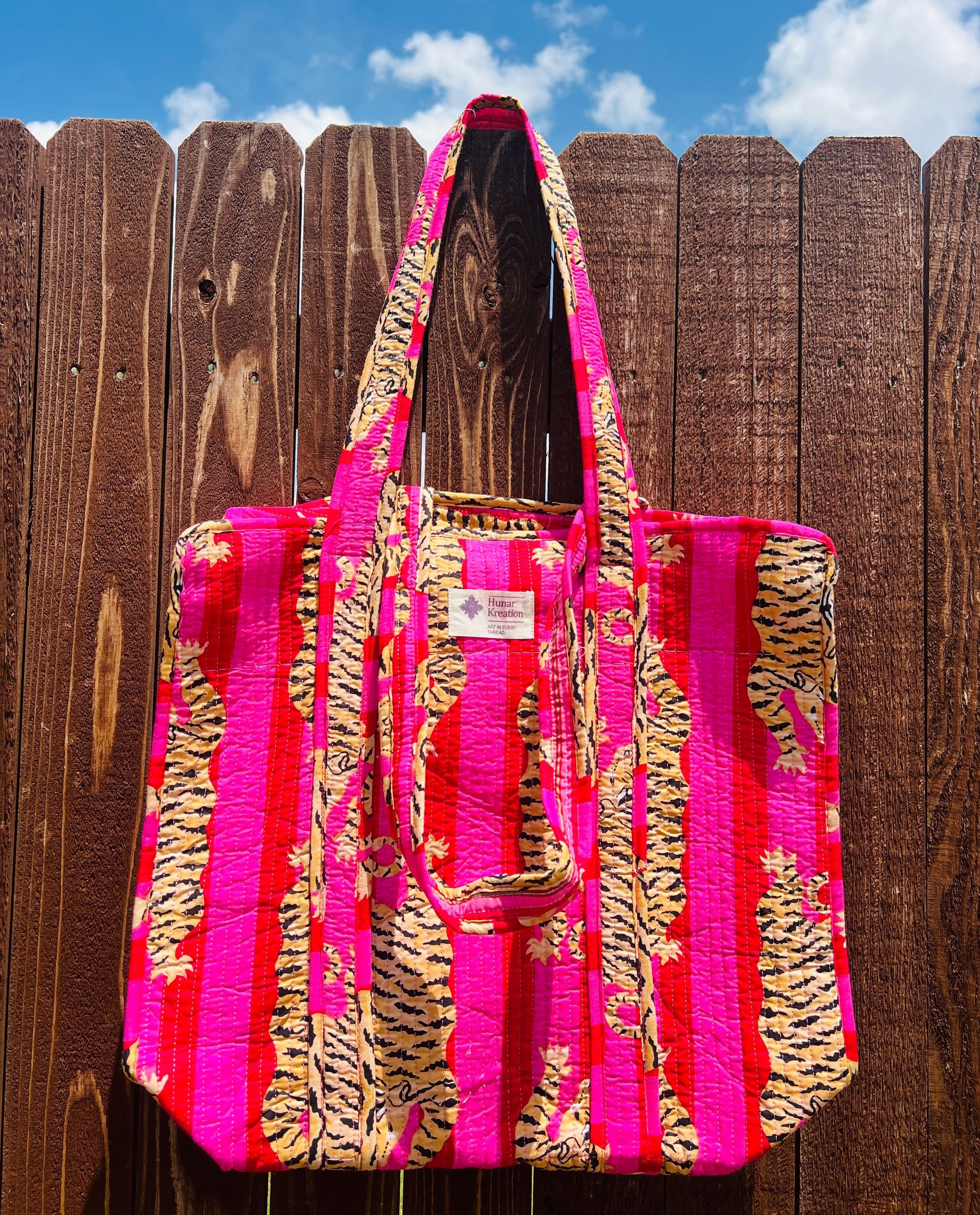 A pink tote bag with a tiger print is sitting on a wooden fence.