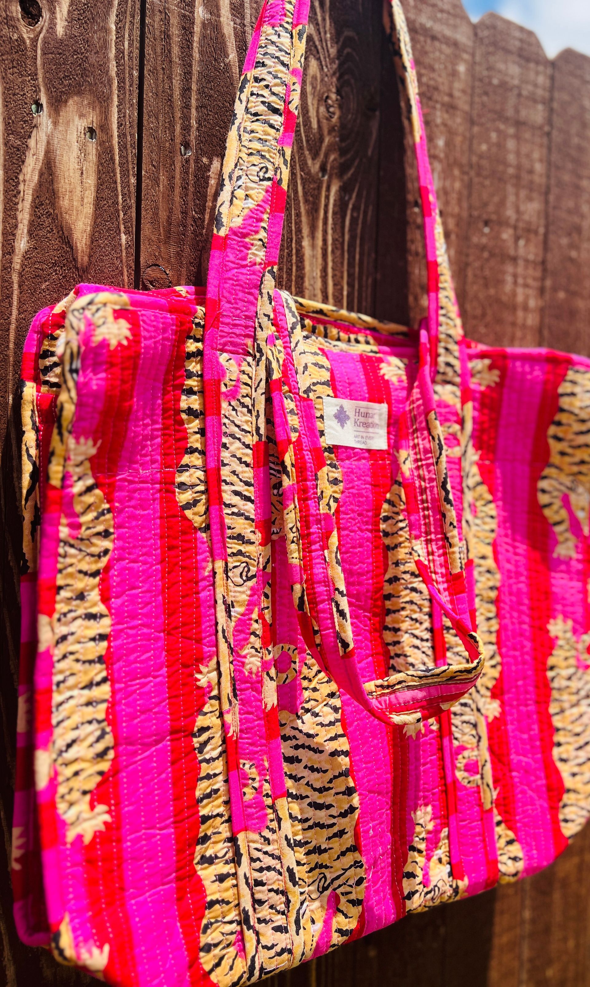 A pink tote bag with a tiger print is sitting on a wooden fence.