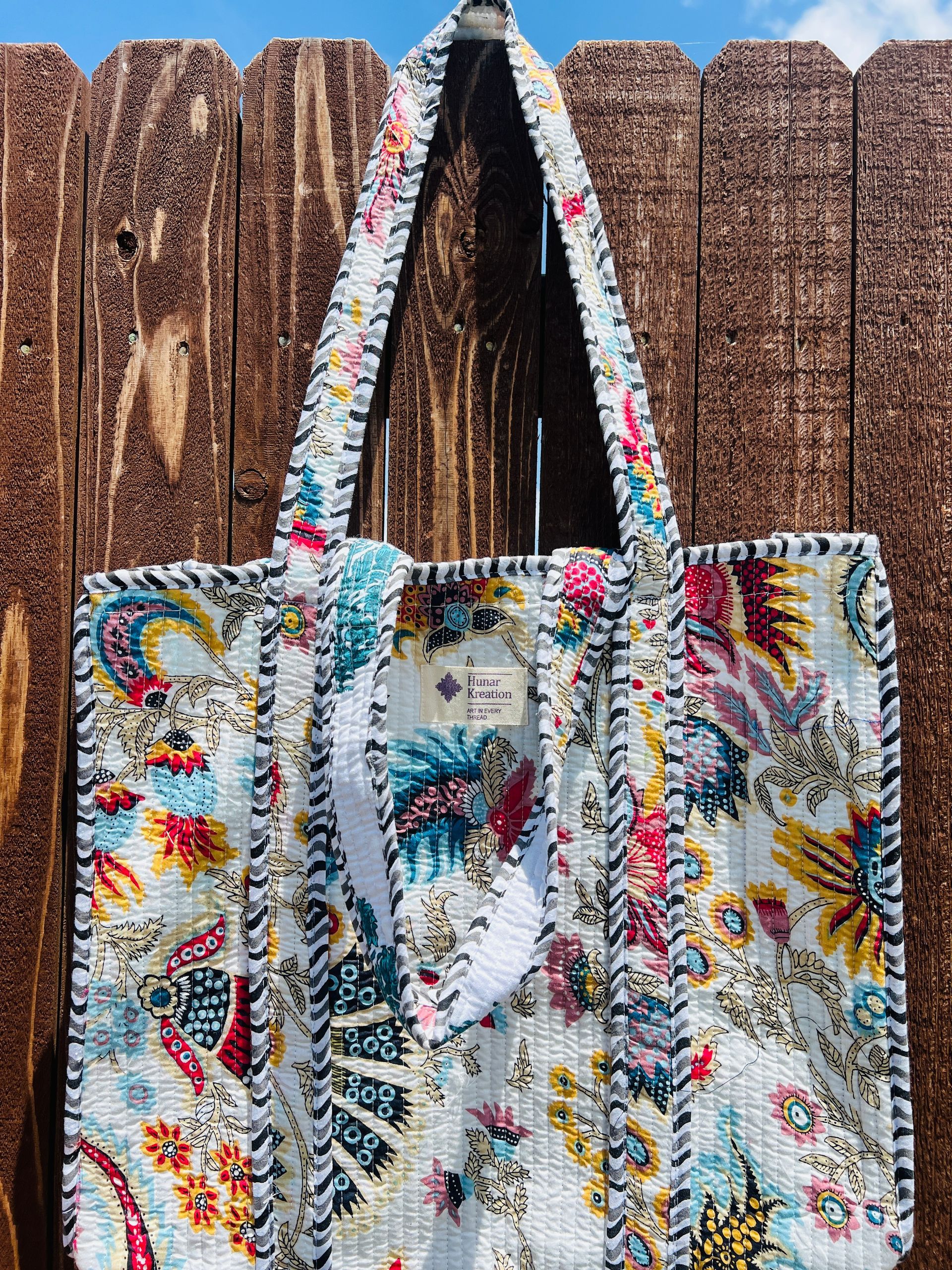 A colorful tote bag is hanging on a wooden fence.