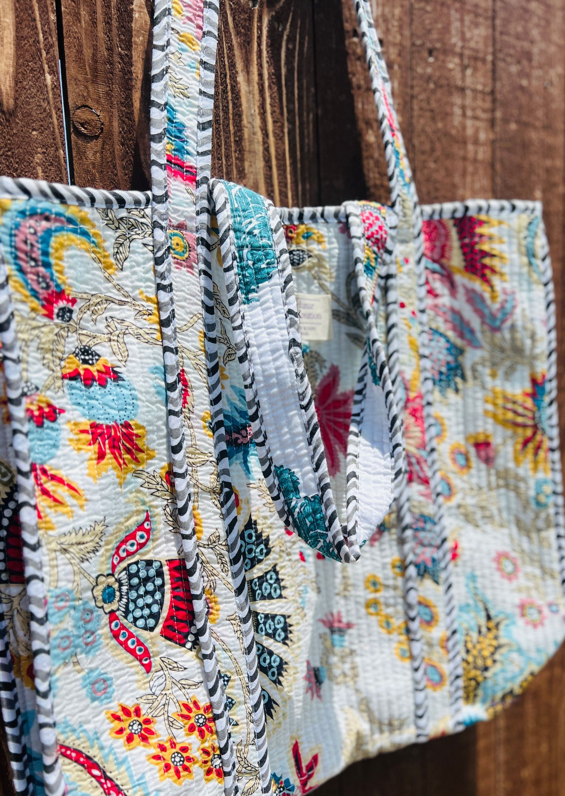 A colorful tote bag is hanging on a wooden fence.