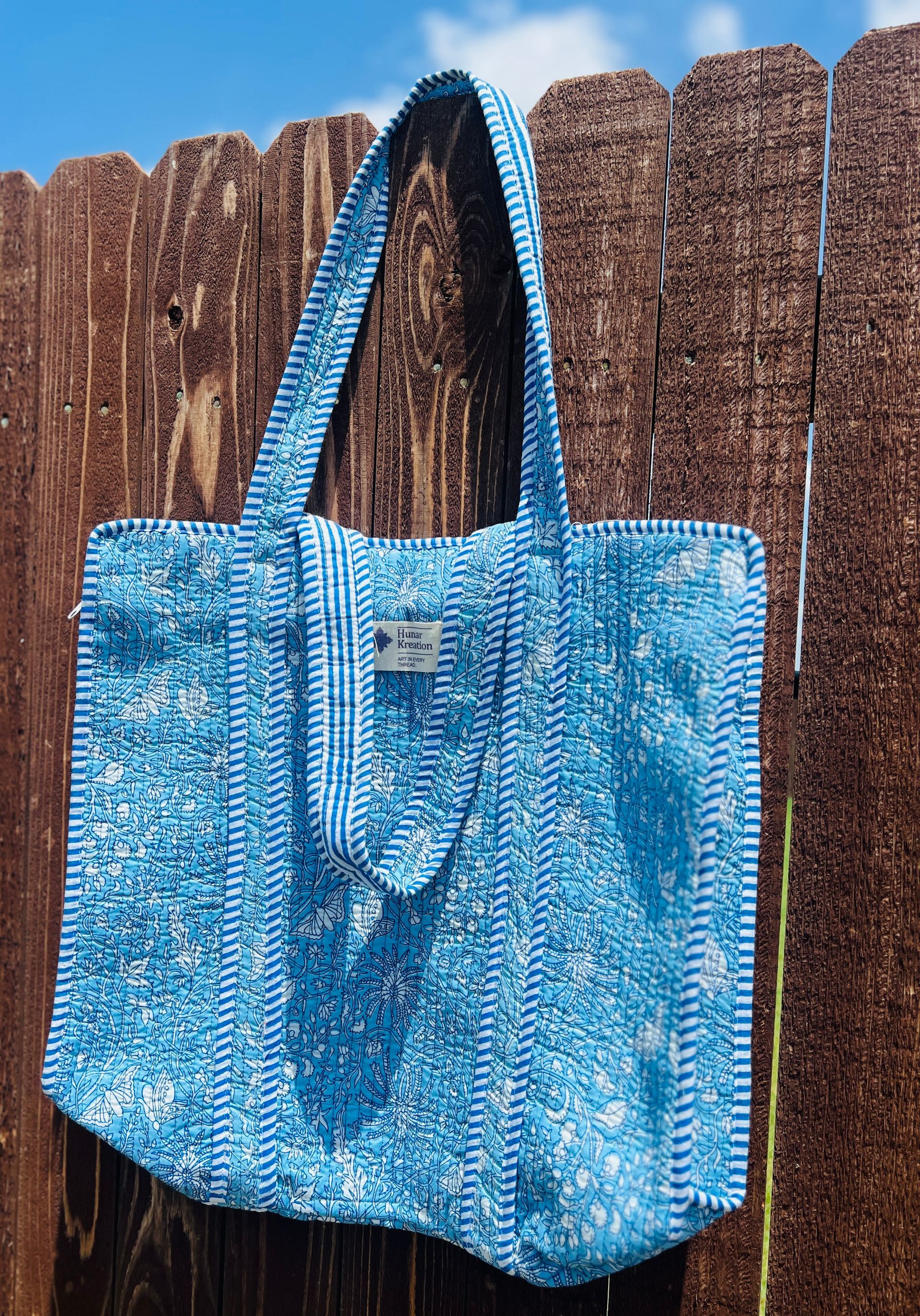 A blue tote bag is hanging on a wooden fence