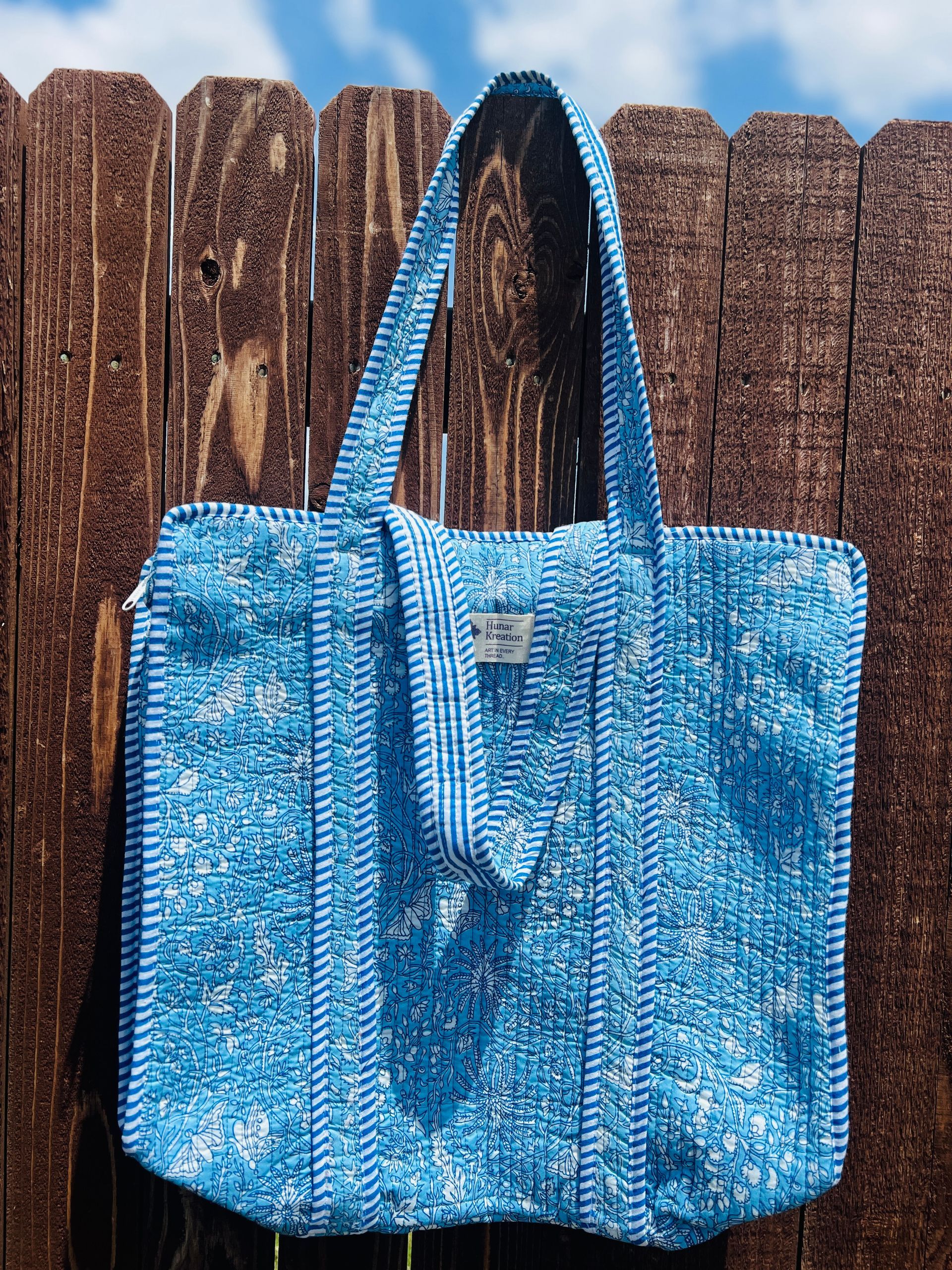 A blue tote bag is hanging on a wooden fence