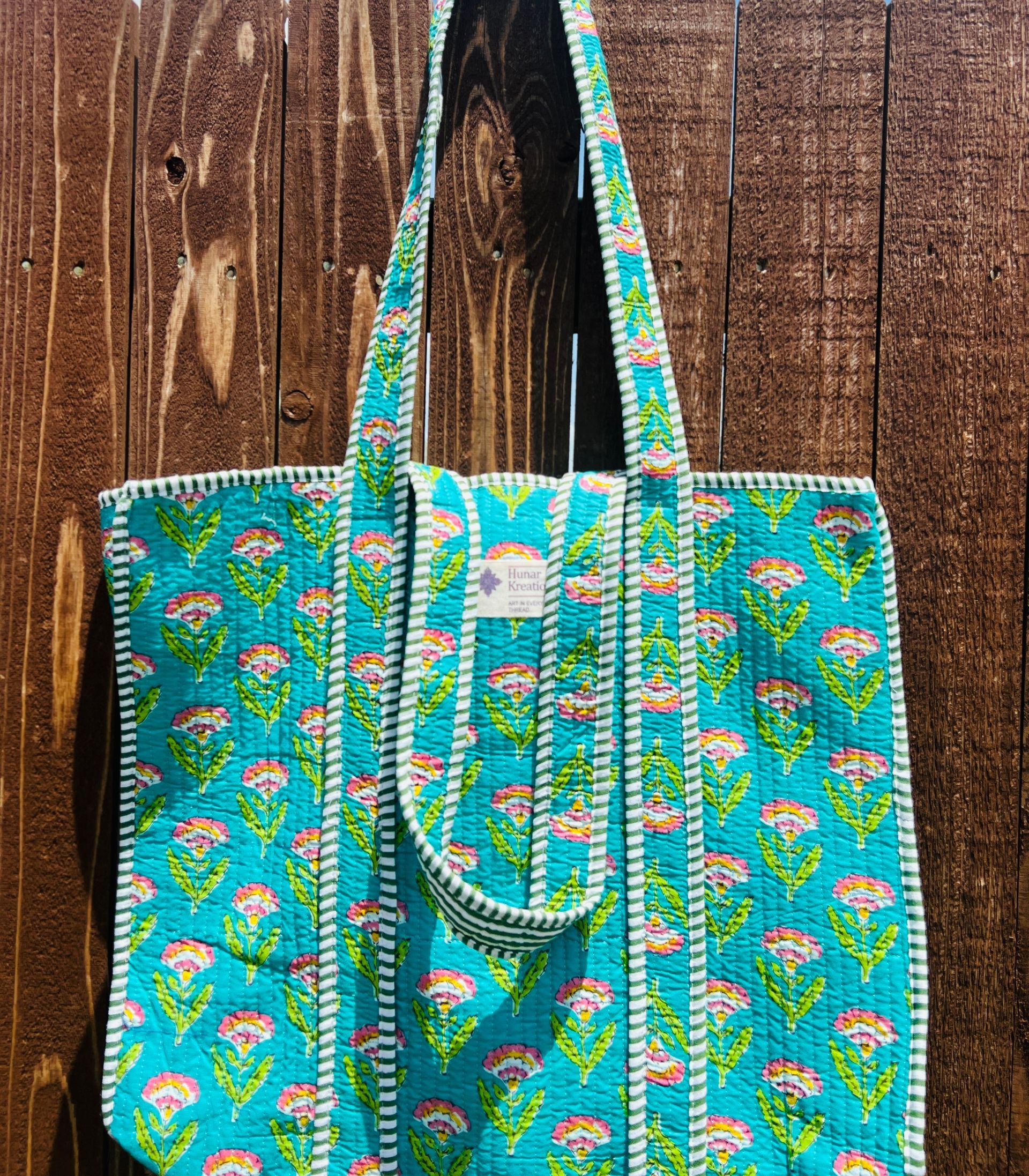 A blue tote bag is hanging on a wooden fence.