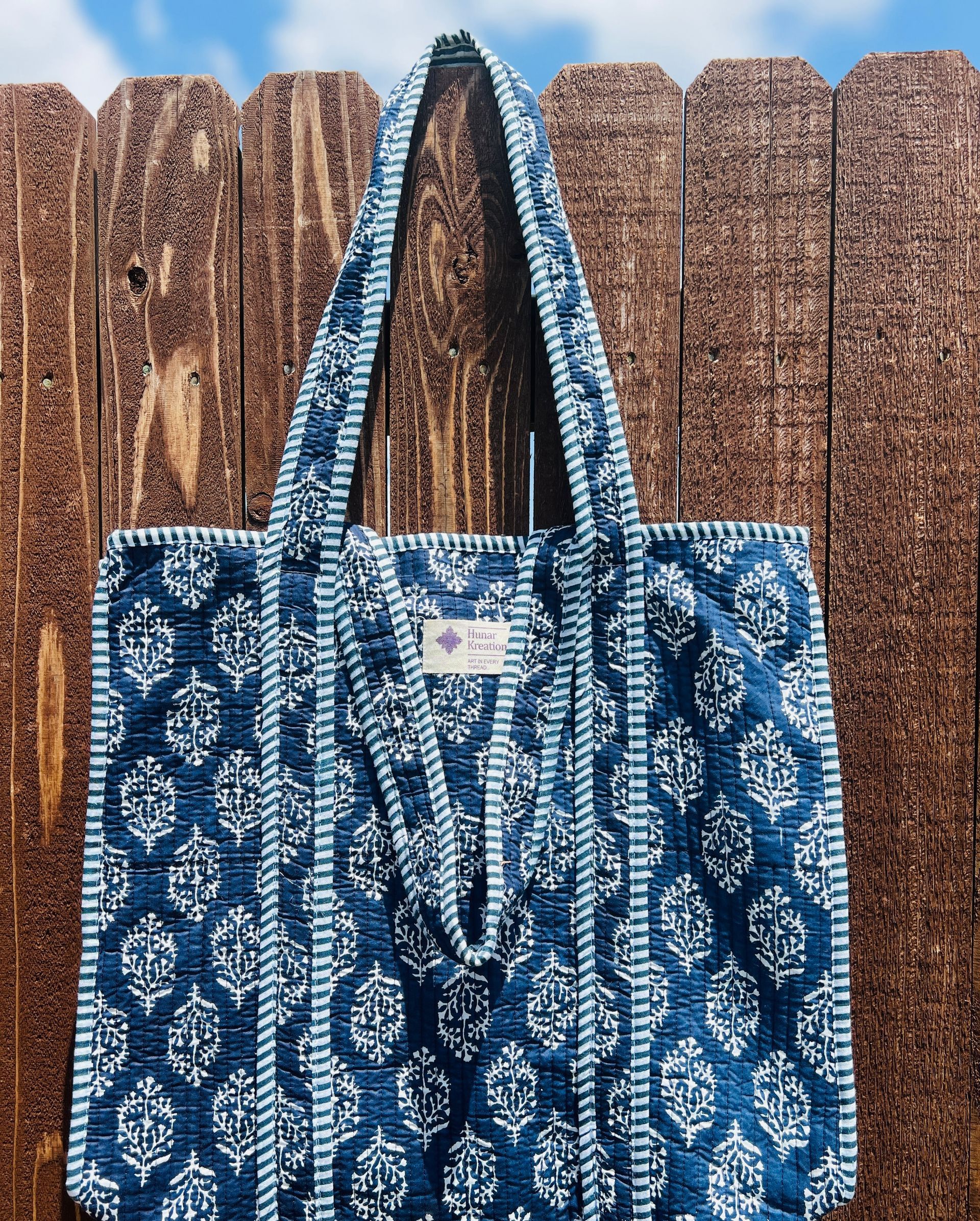A blue and white tote bag is hanging on a wooden fence