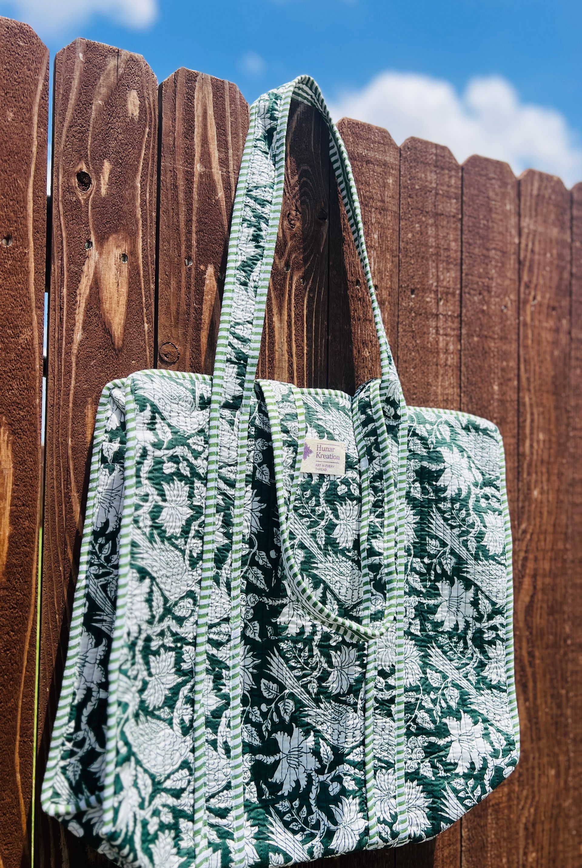 A green and white tote bag is hanging on a wooden fence.