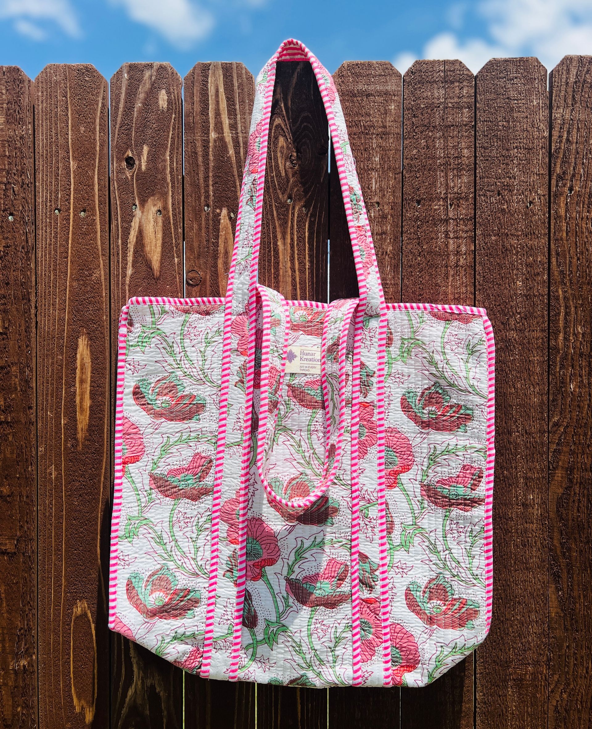 A pink and white tote bag is hanging on a wooden fence.