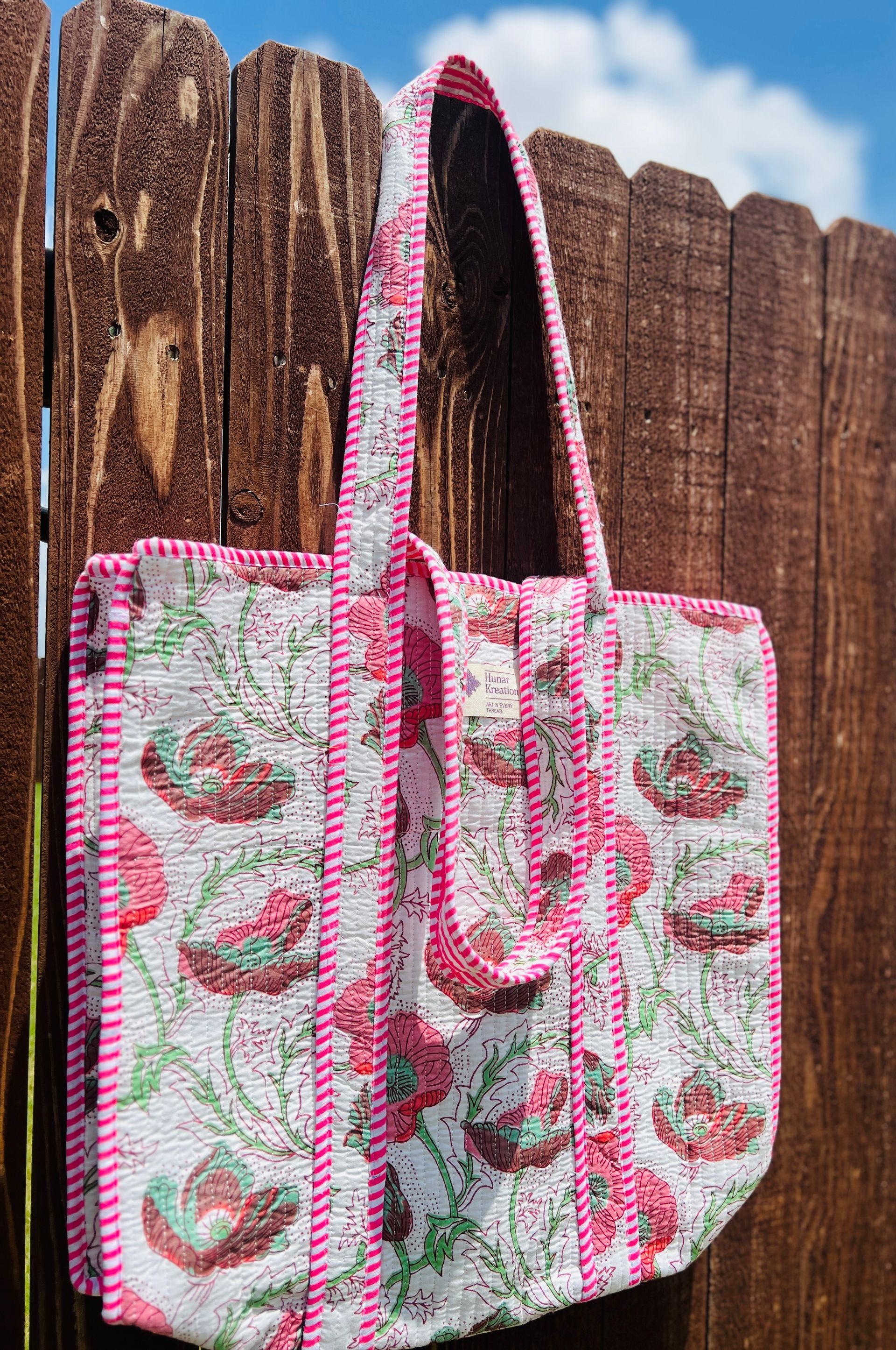A pink and white tote bag is hanging on a wooden fence.