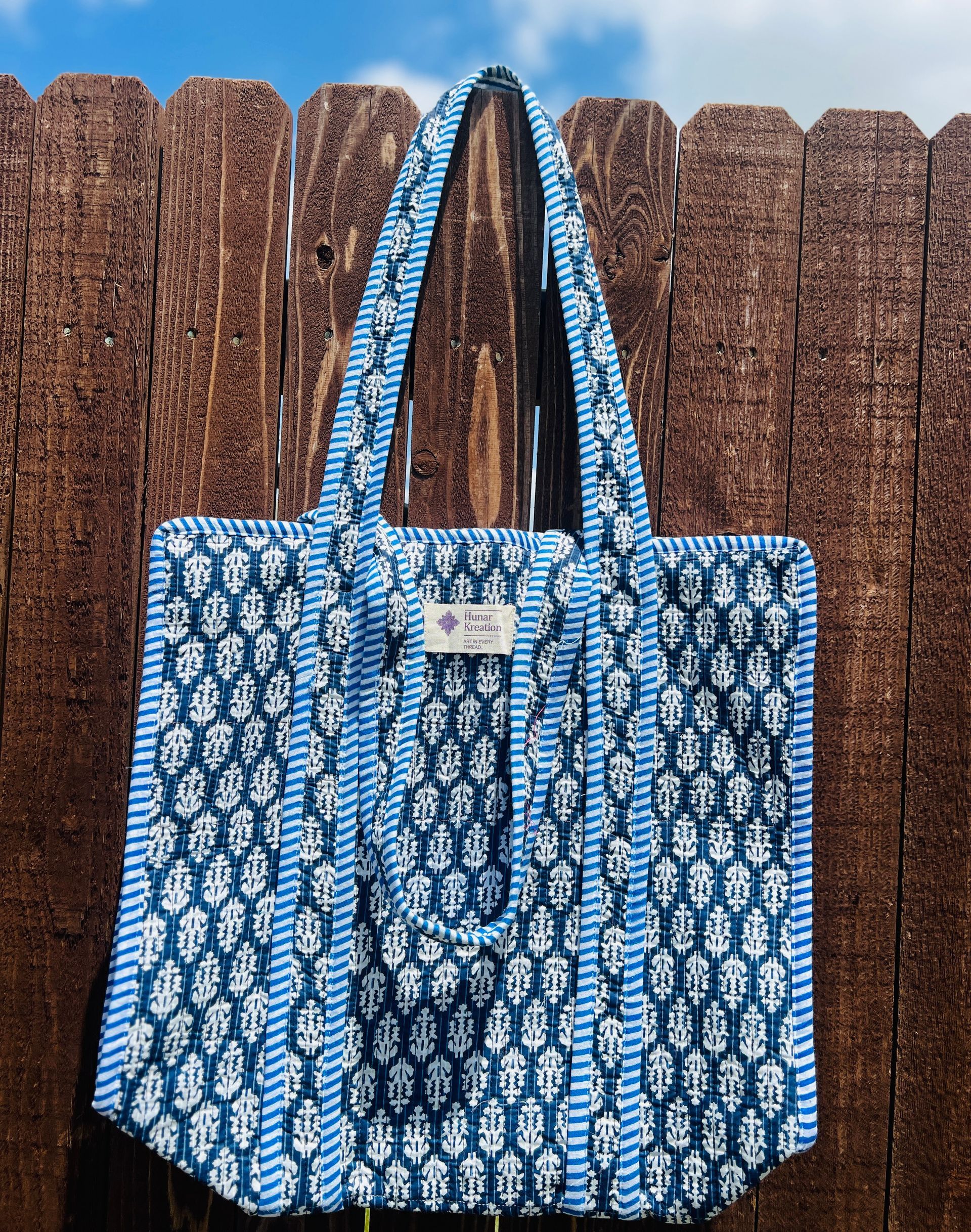 A blue and white tote bag is hanging on a wooden fence