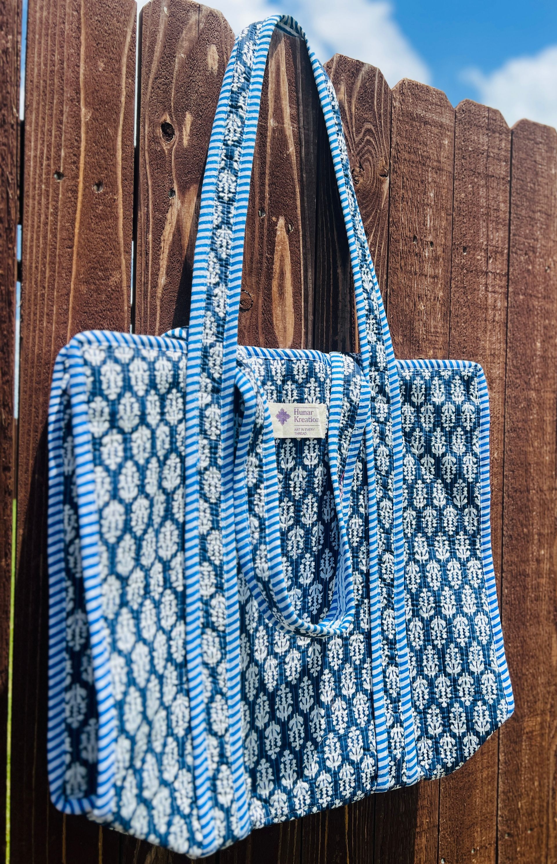 A blue and white tote bag is hanging on a wooden fence