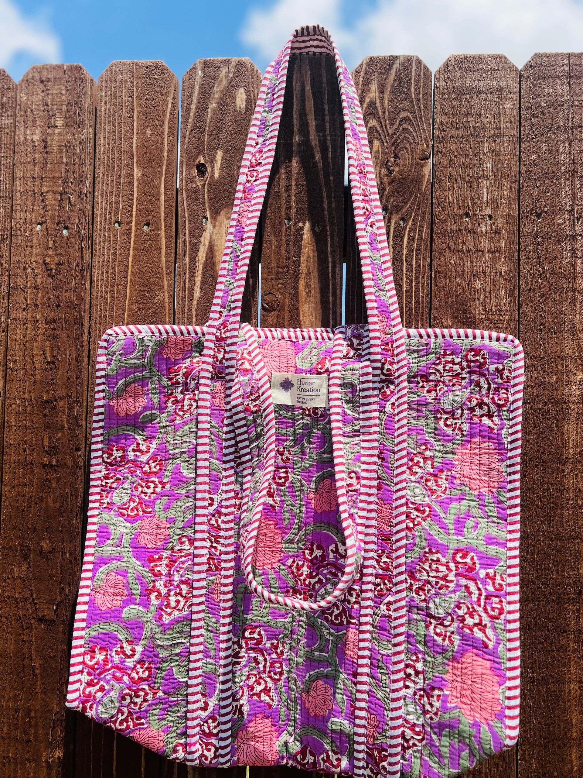 A purple tote bag is hanging on a wooden fence