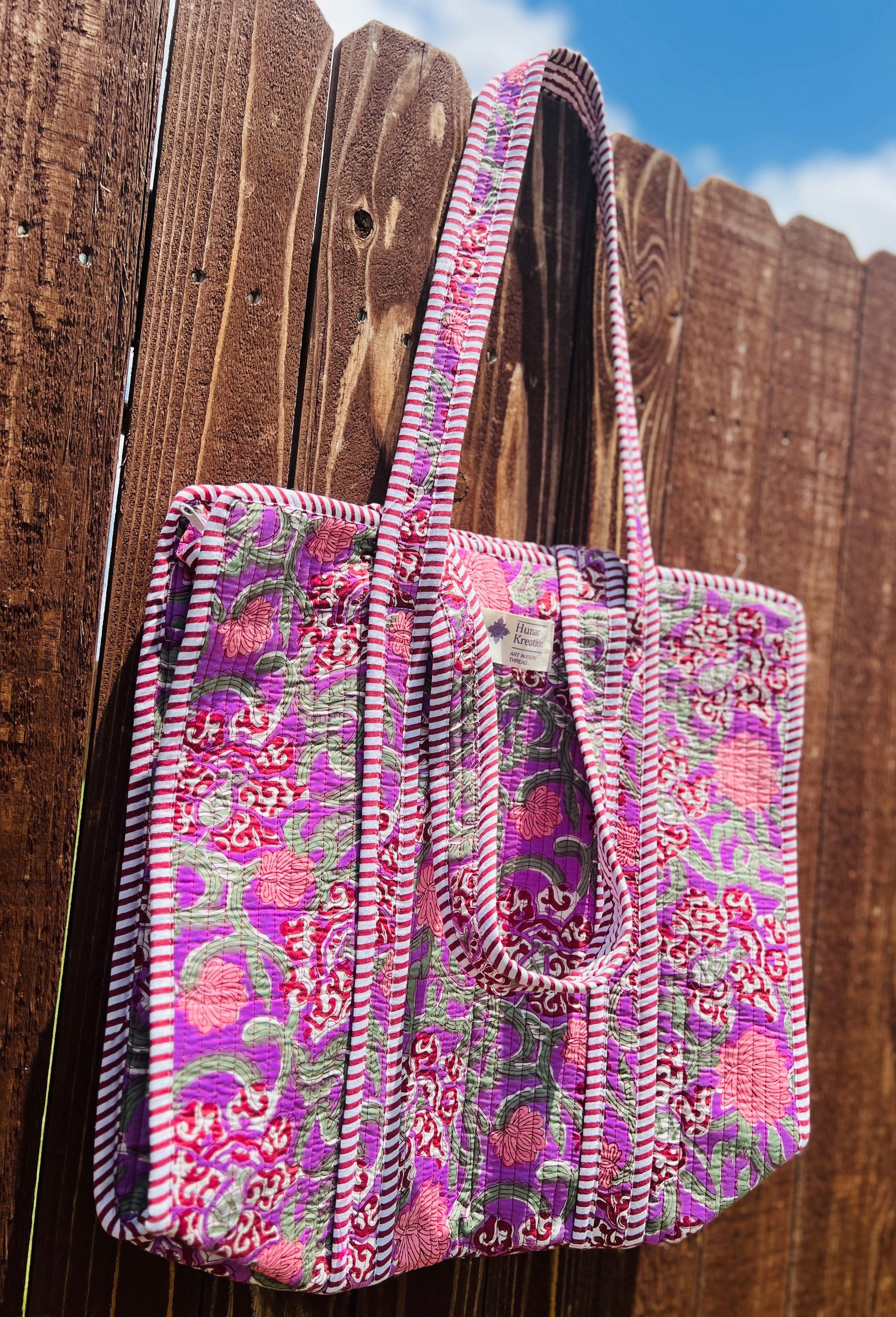 A purple tote bag is hanging on a wooden fence