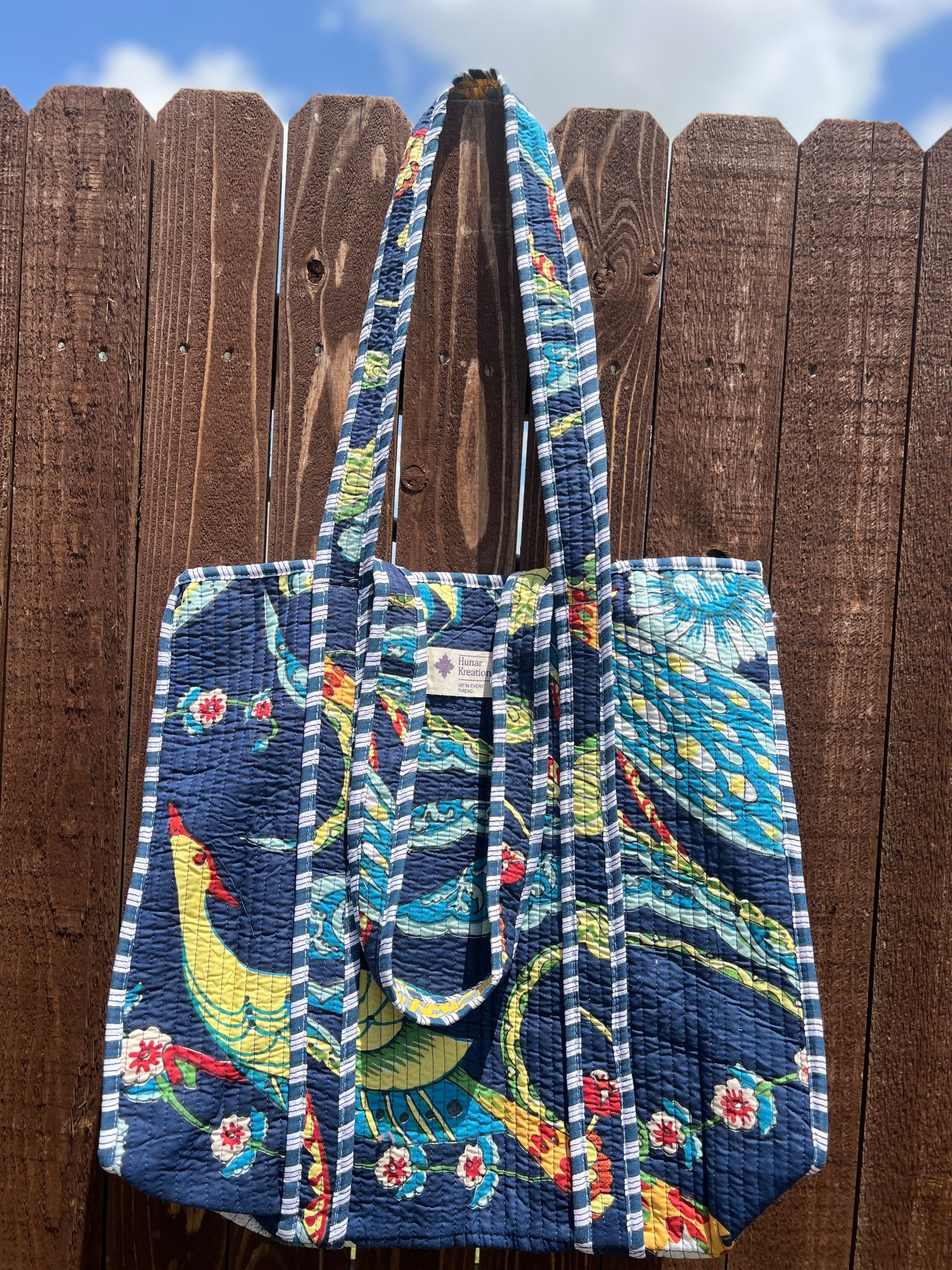 A blue tote bag is hanging on a wooden fence.
