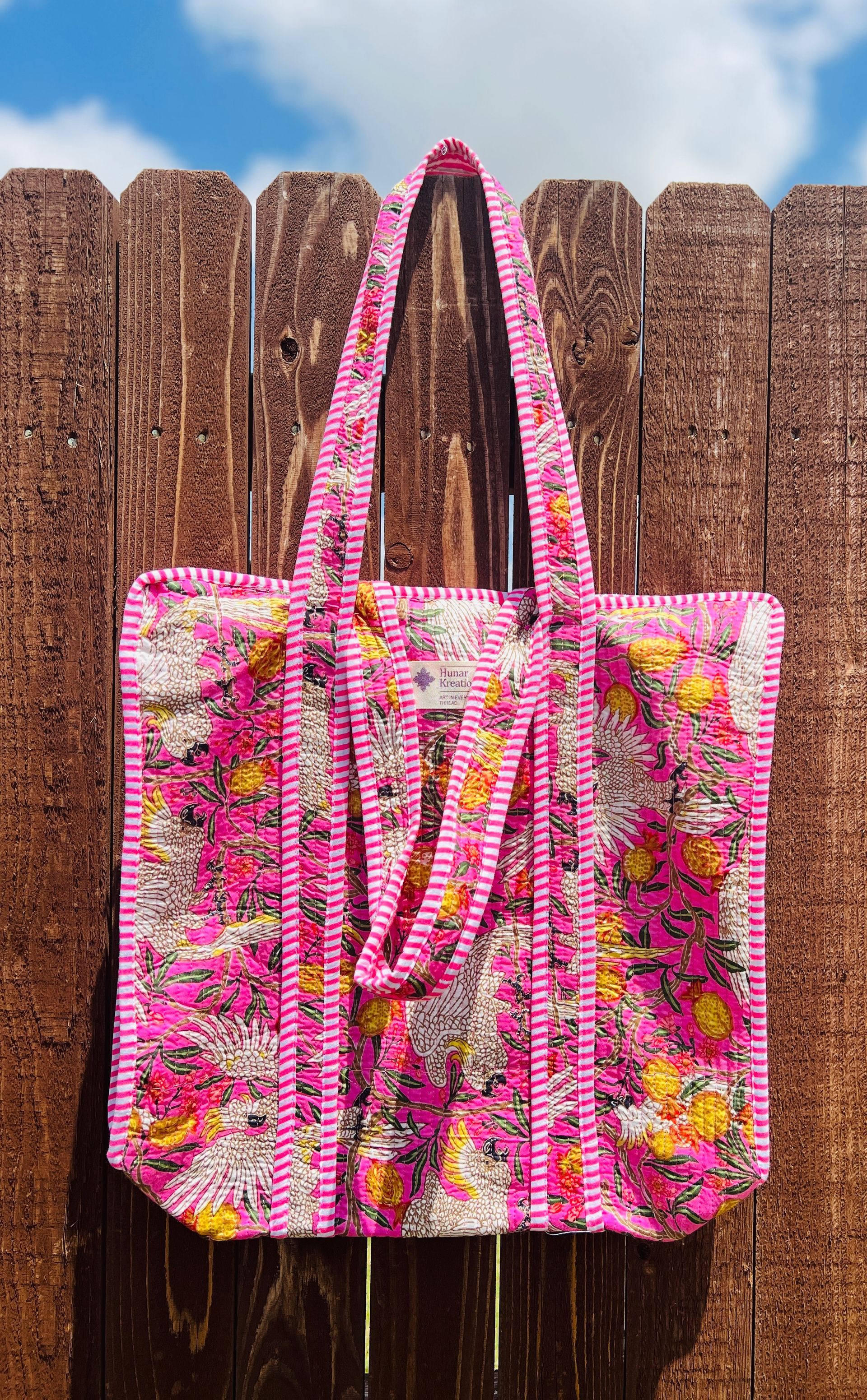 A pink tote bag is hanging on a wooden fence.