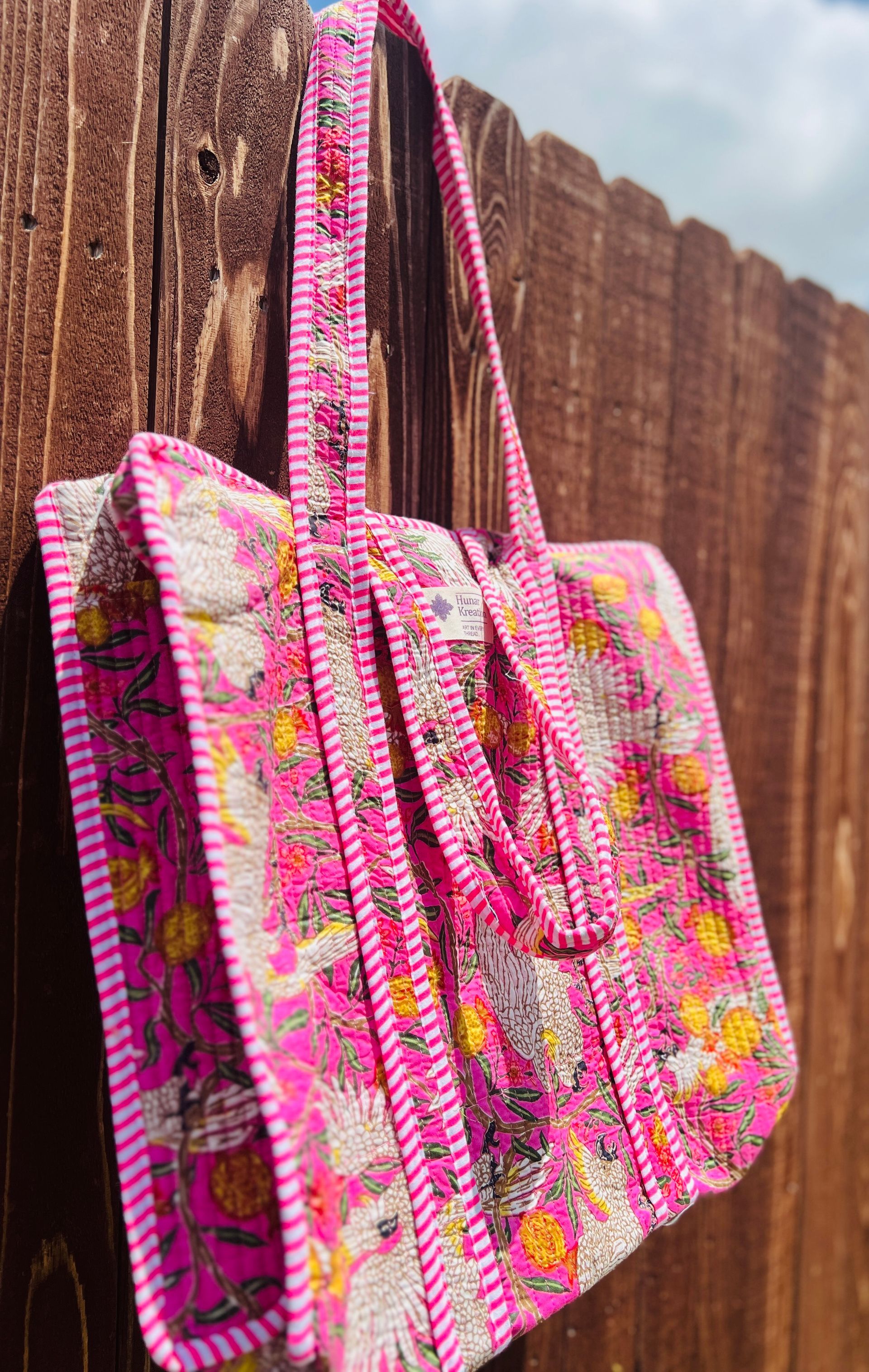 A pink tote bag is hanging on a wooden fence.