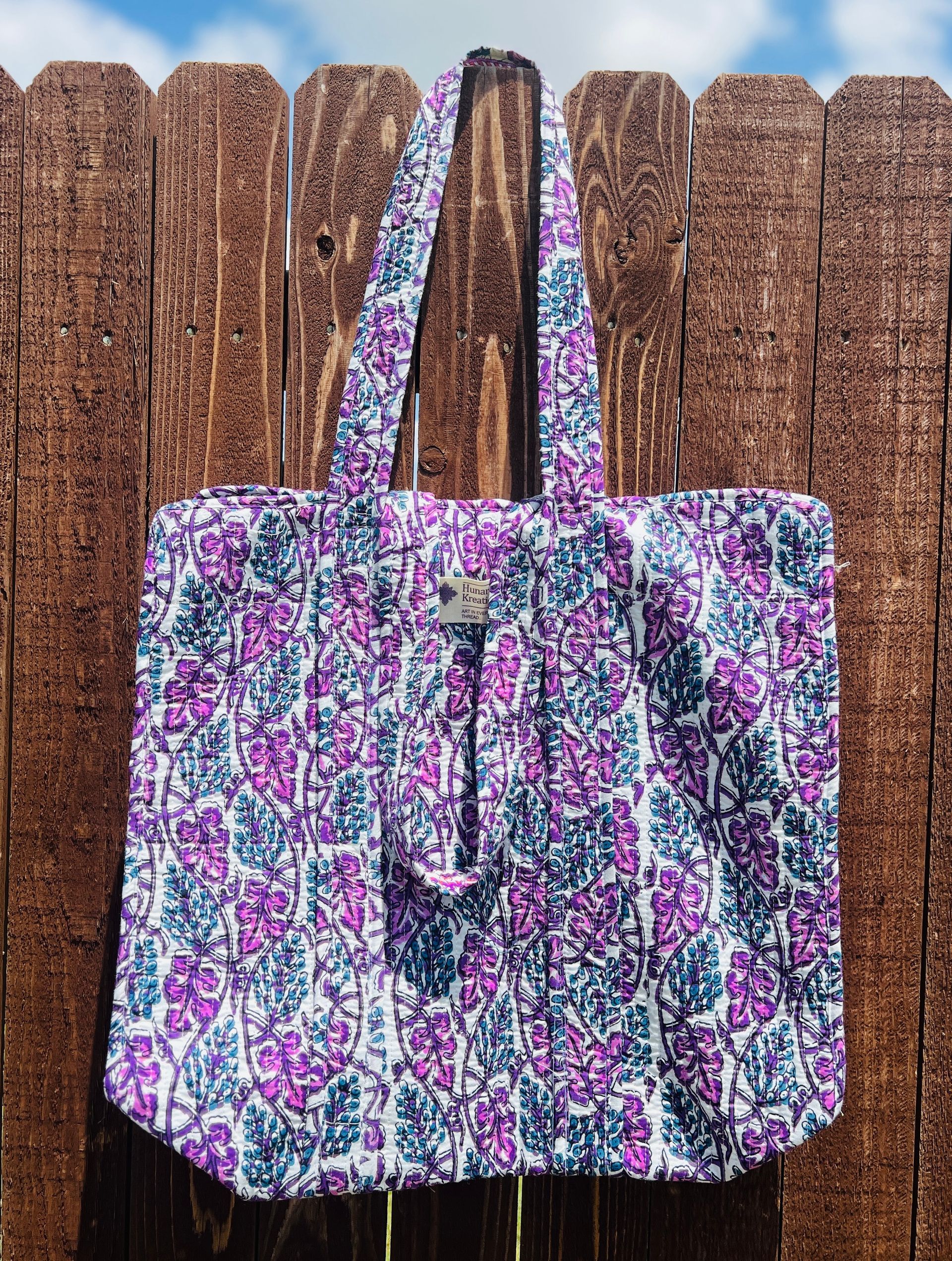 A purple and blue tote bag is hanging on a wooden fence