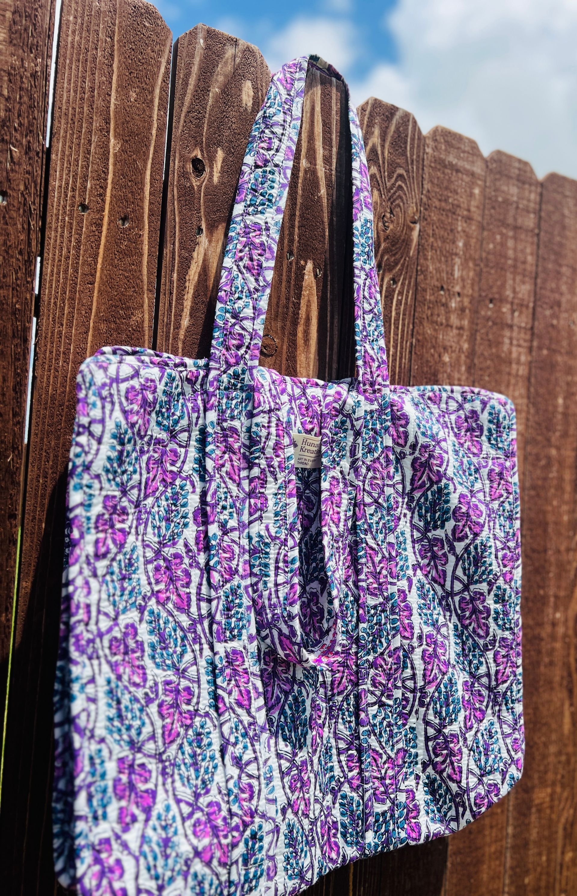 A purple and blue tote bag is hanging on a wooden fence