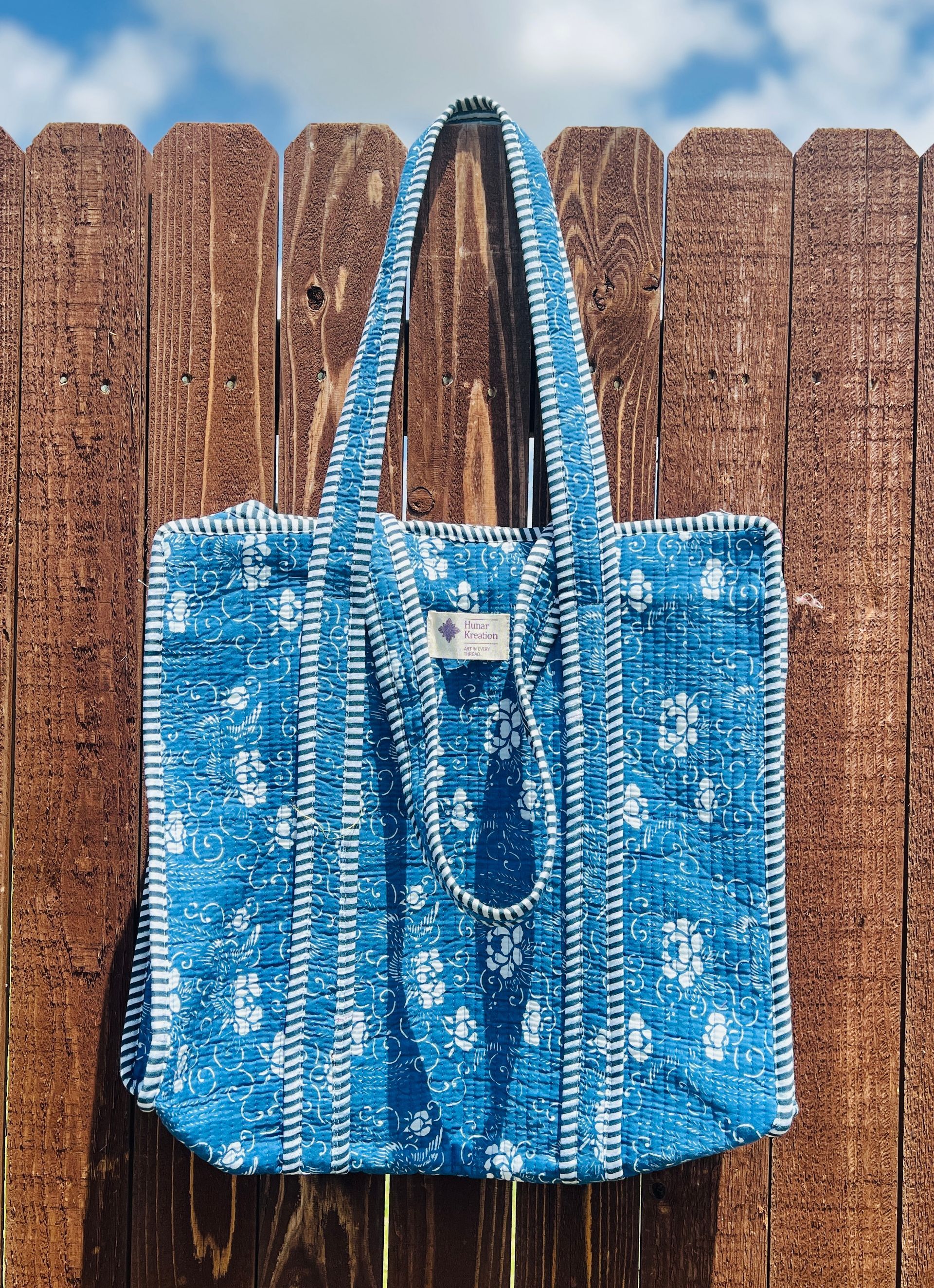 A blue tote bag is hanging on a wooden fence.