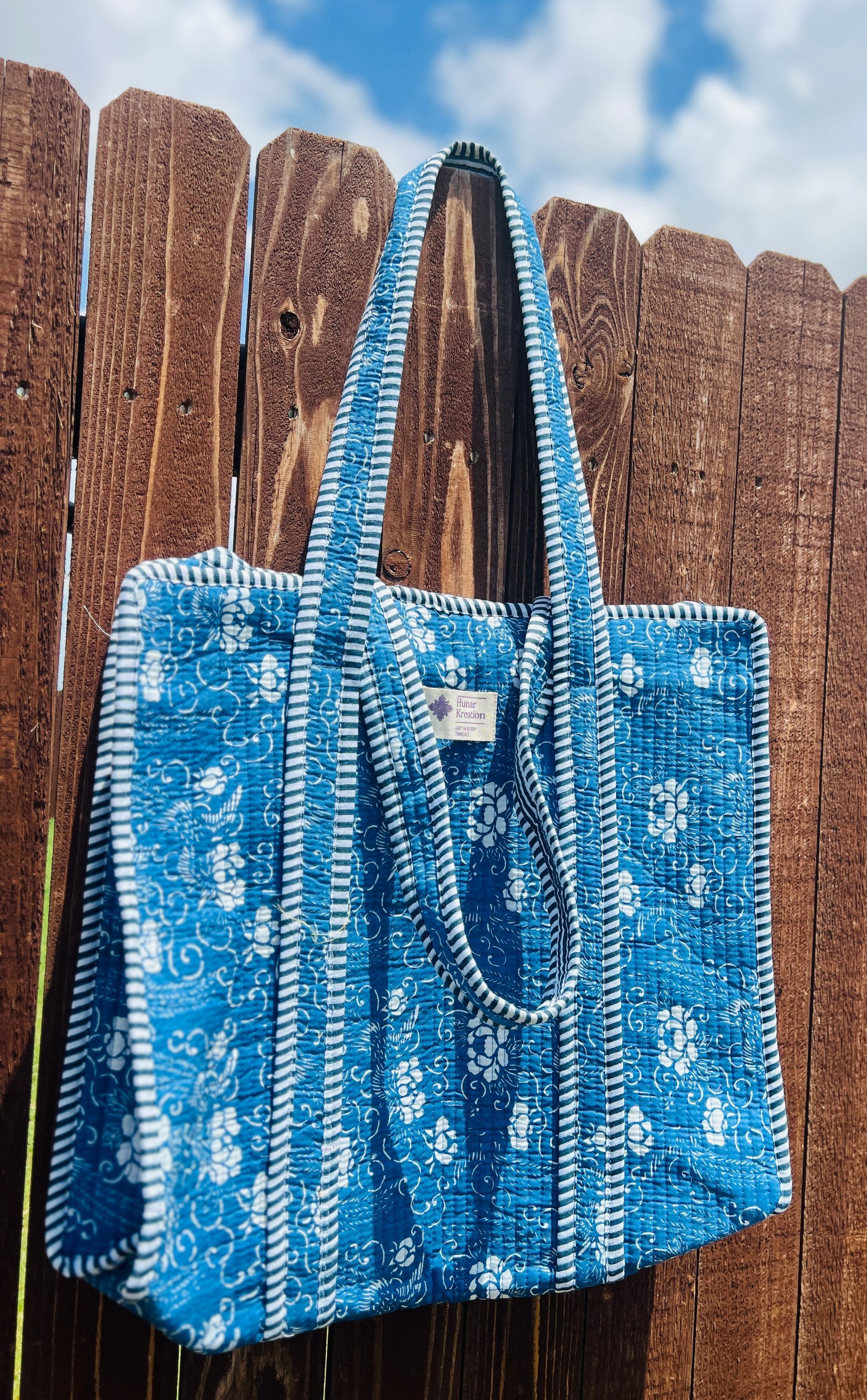 A blue tote bag is hanging on a wooden fence.