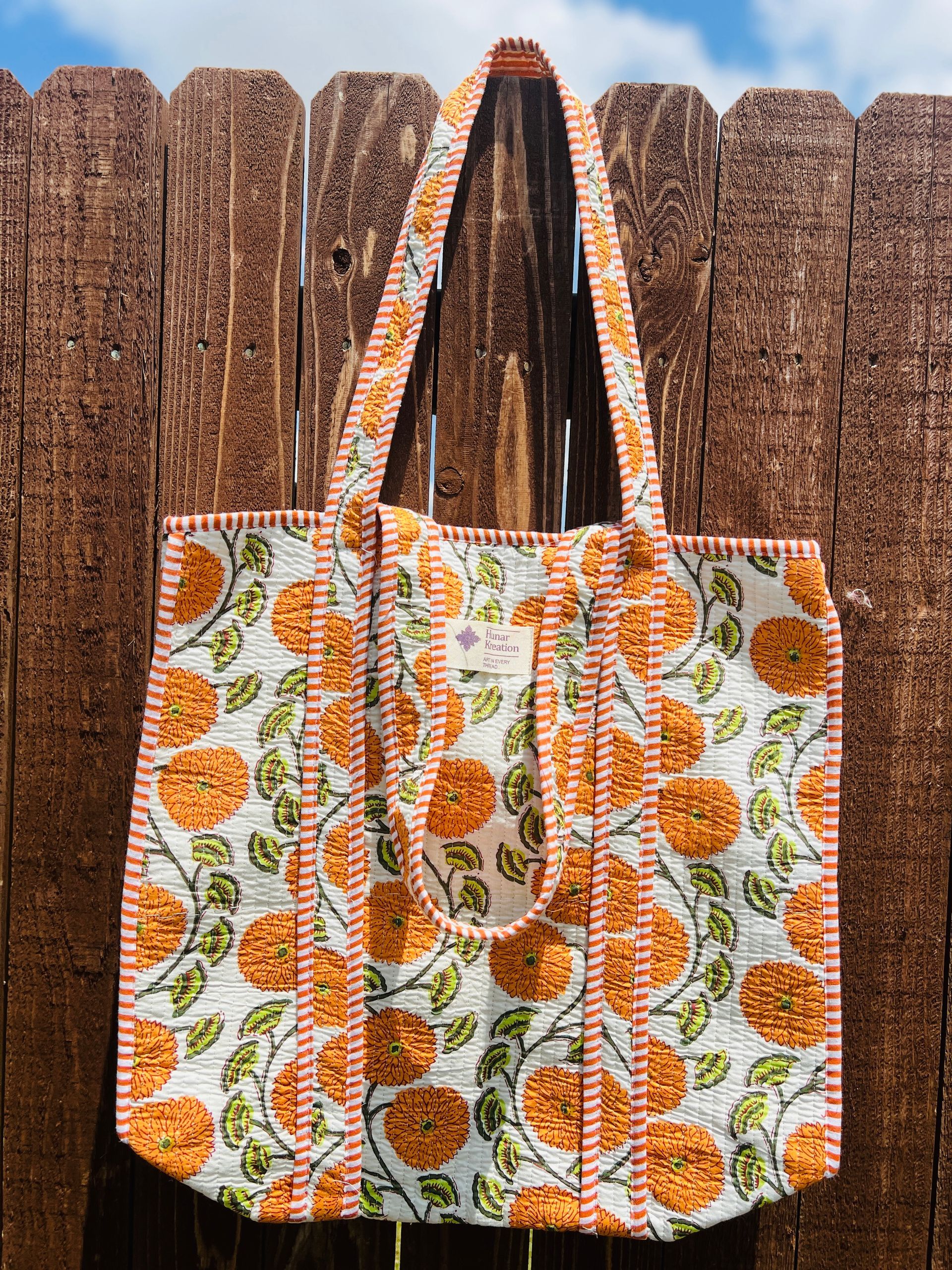 A tote bag is hanging on a wooden fence.
